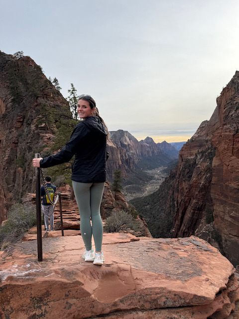 Woman standing at Angels Landing summit overlooking Zion Canyon at dusk