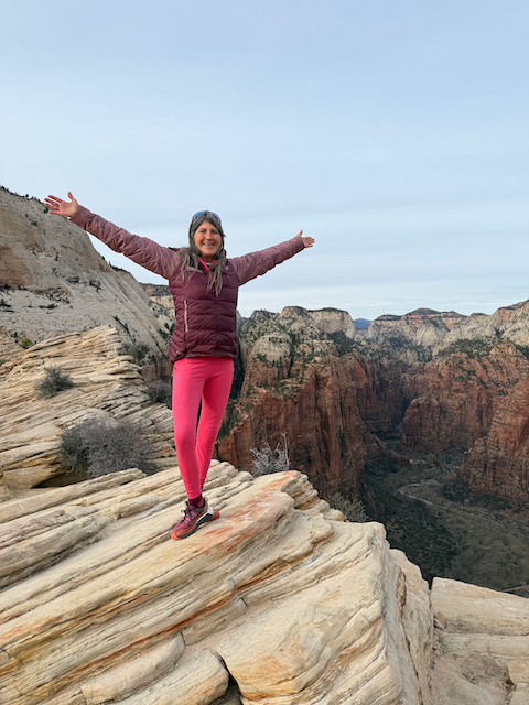 Woman with arms wide open standing triumphantly on Angels Landing summit
