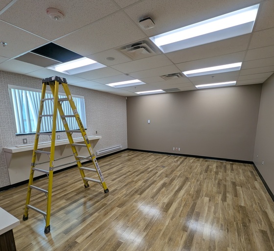 Commercial office space undergoing tenant improvement painting in Saskatoon with a stepladder on a wood floor and freshly painted walls during a business buildout