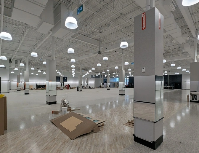 Large open-concept commercial space interior during renovation, featuring high industrial ceilings, polished floors, and structural columns with mirrored panels