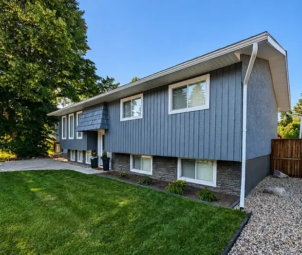 A residential exterior home painting project featuring a blue-grey vertical wood-paneled siding and stone masonry foundation