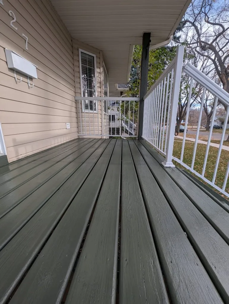 A view of a freshly painted sage green wooden front porch deck on a beige house with white railings