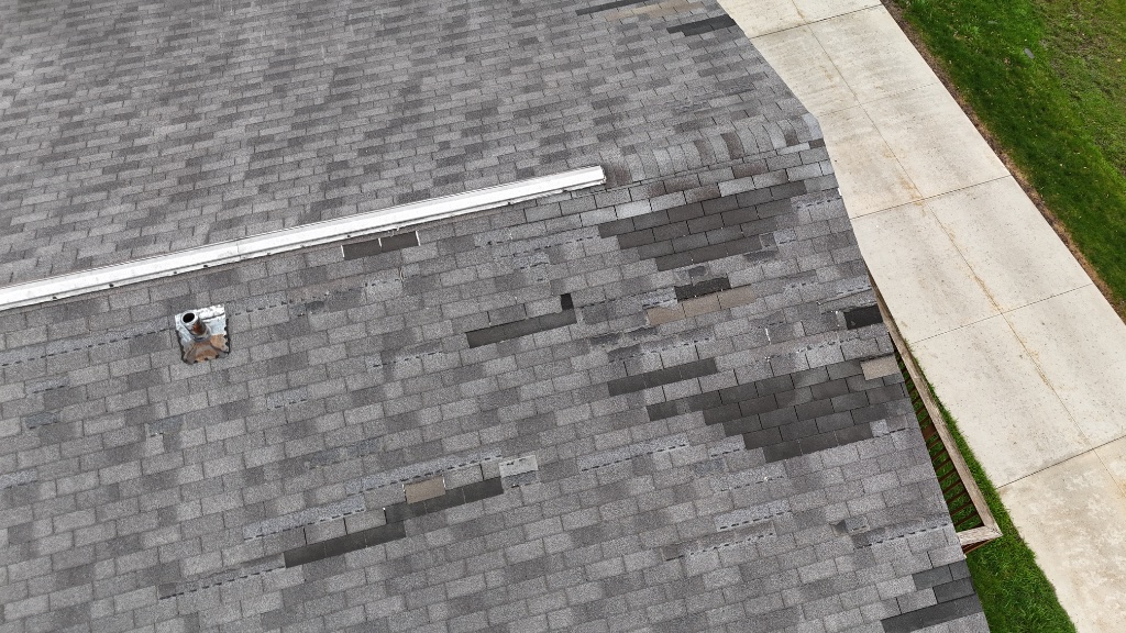 Aerial view of wind-damaged shingles — missing and lifted across the roof
