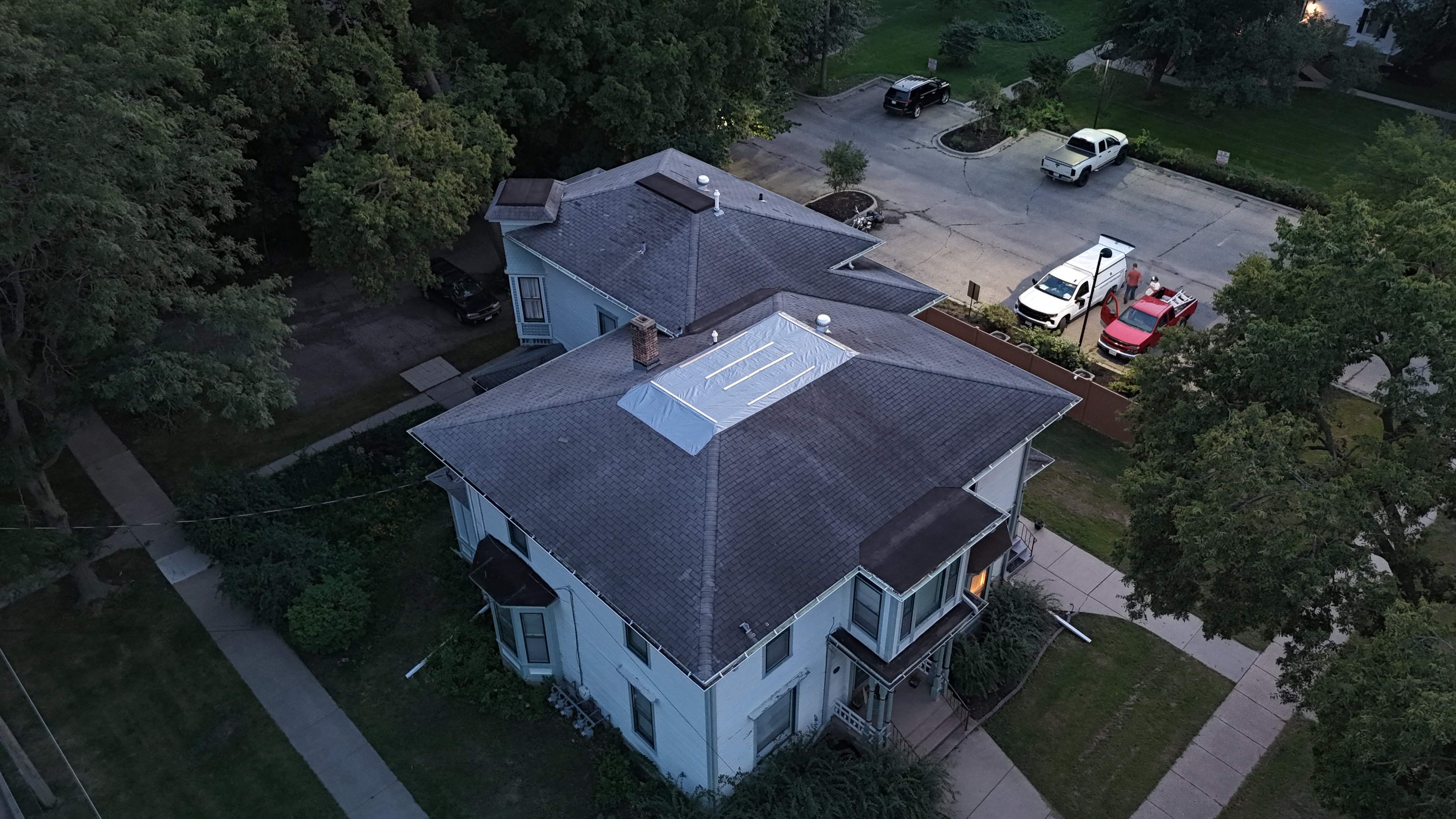 Aerial view of house at dusk with tarp secured over the repaired roof section