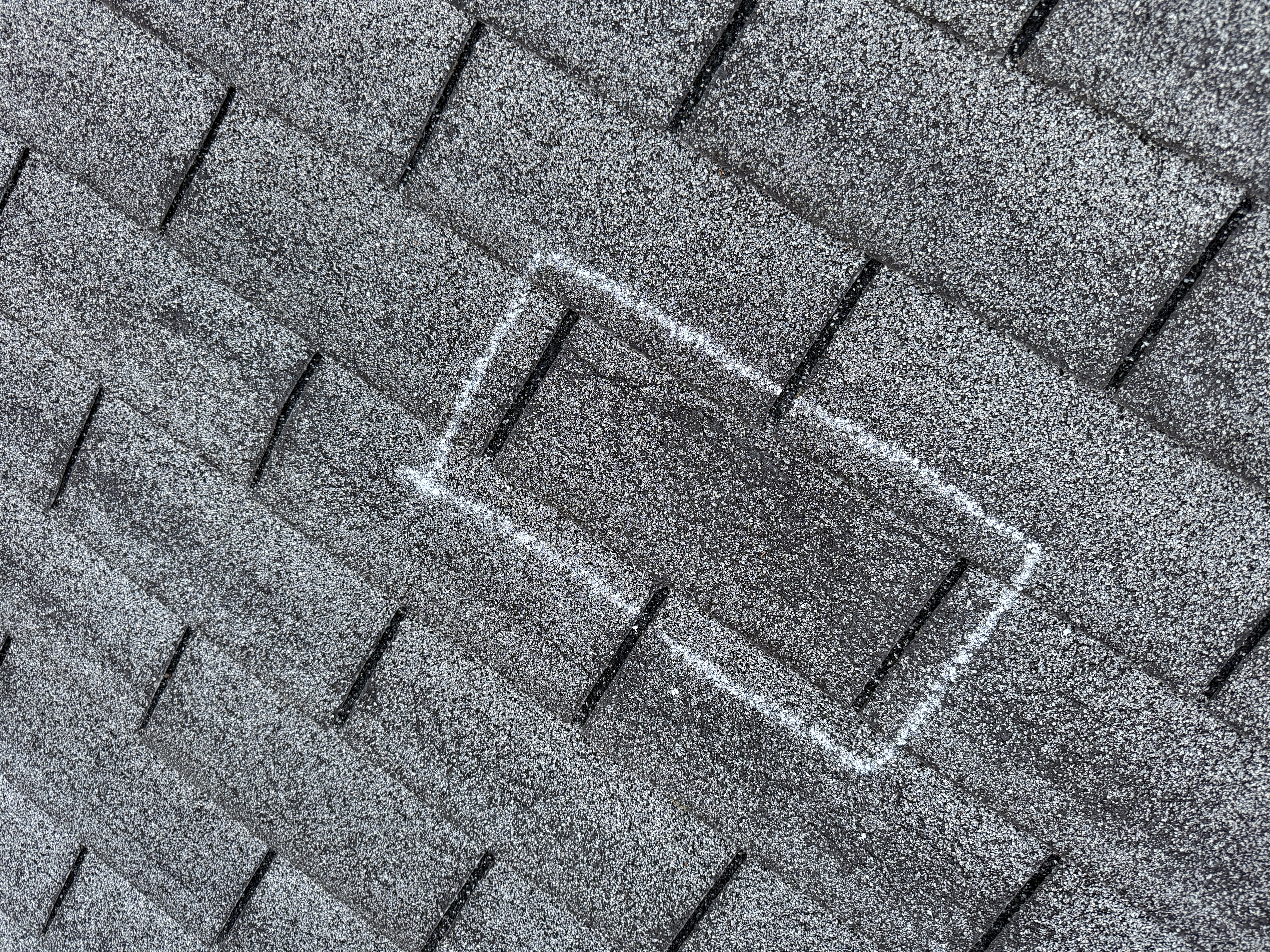 Chalk-outlined shingle on a frosty roof showing the seal has released and begun to crease