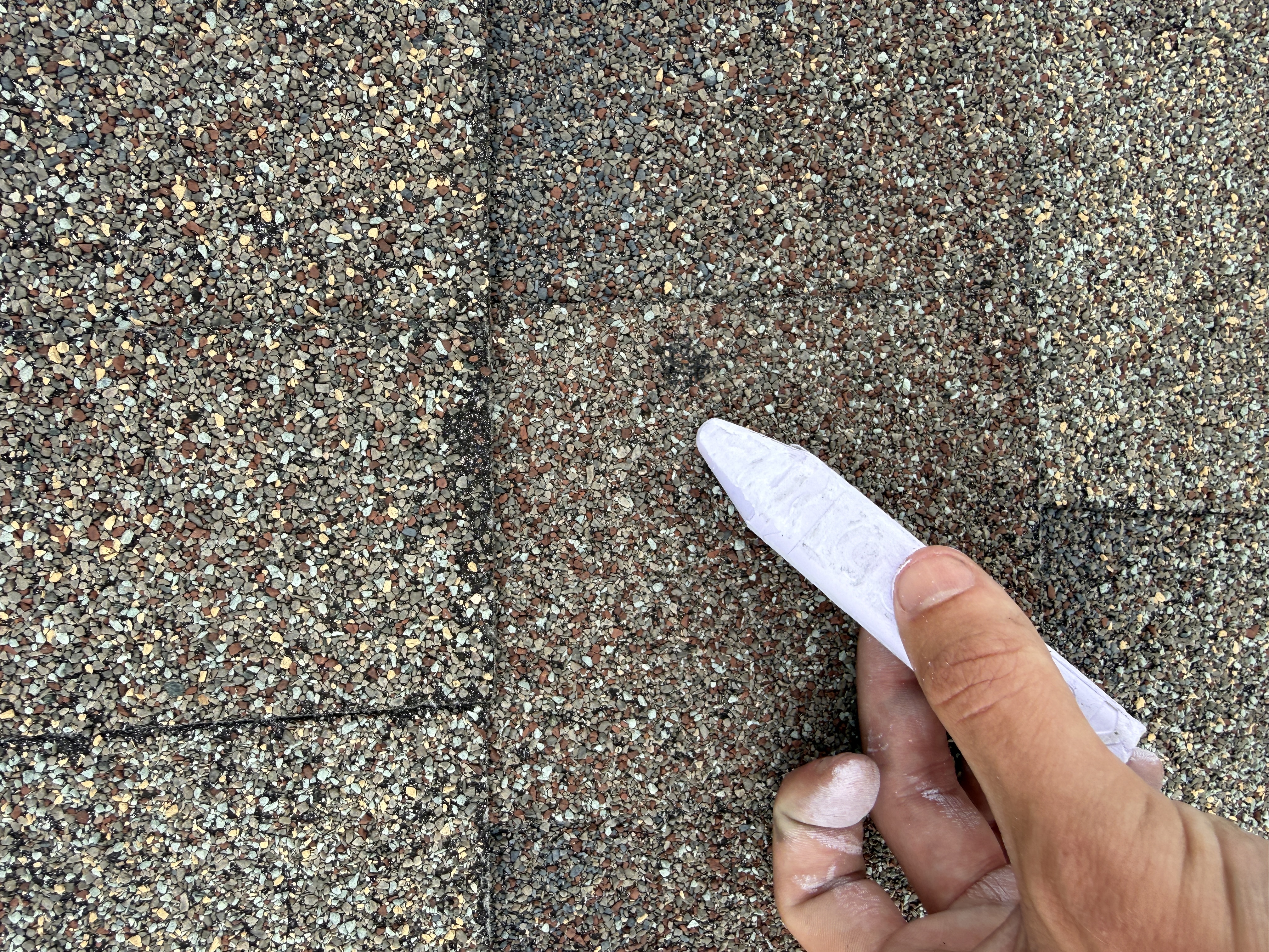 Hand holding chalk over a hail-impacted shingle