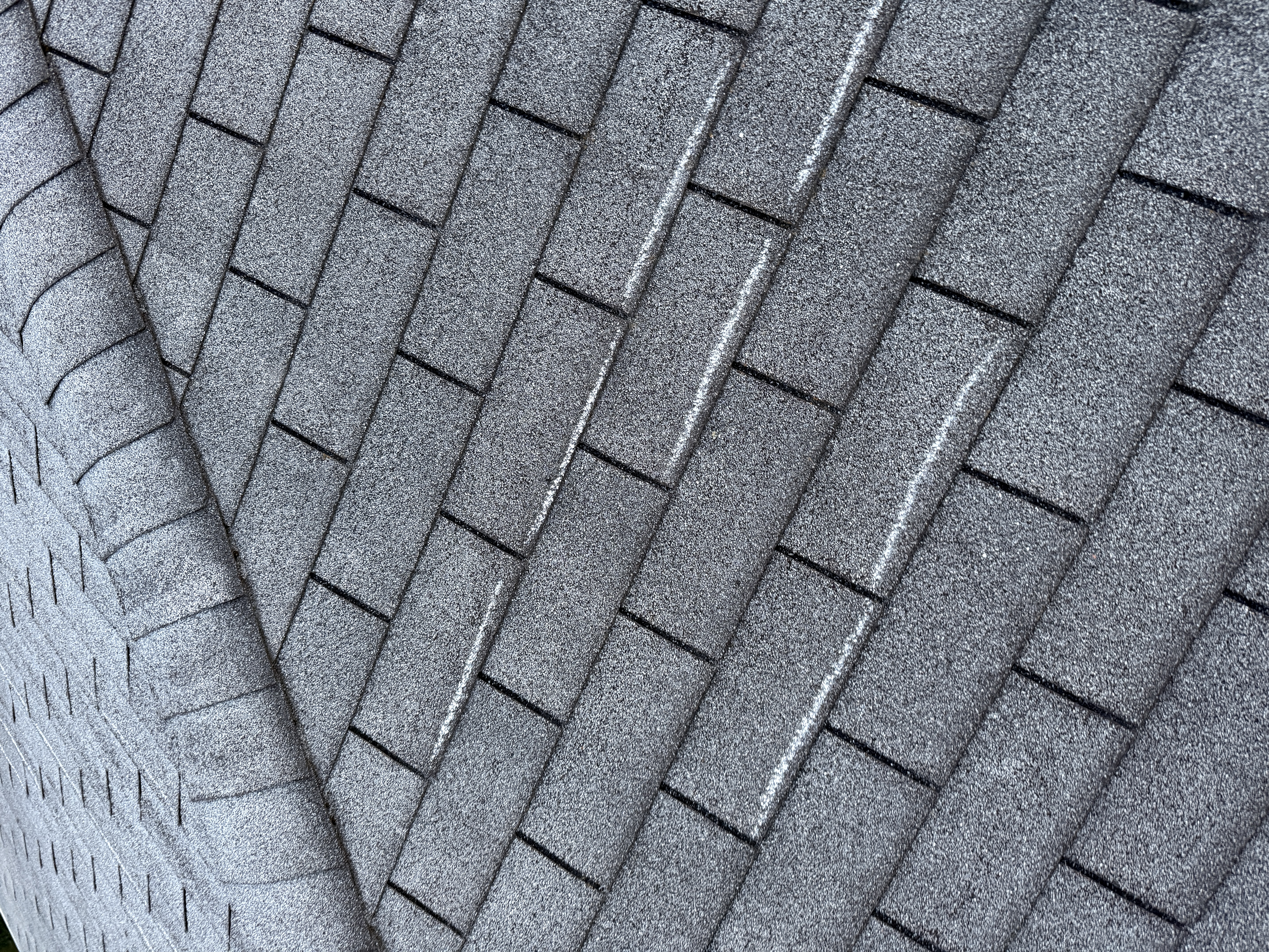 Close-up of a horizontal crease line across the face of dark gray architectural shingles