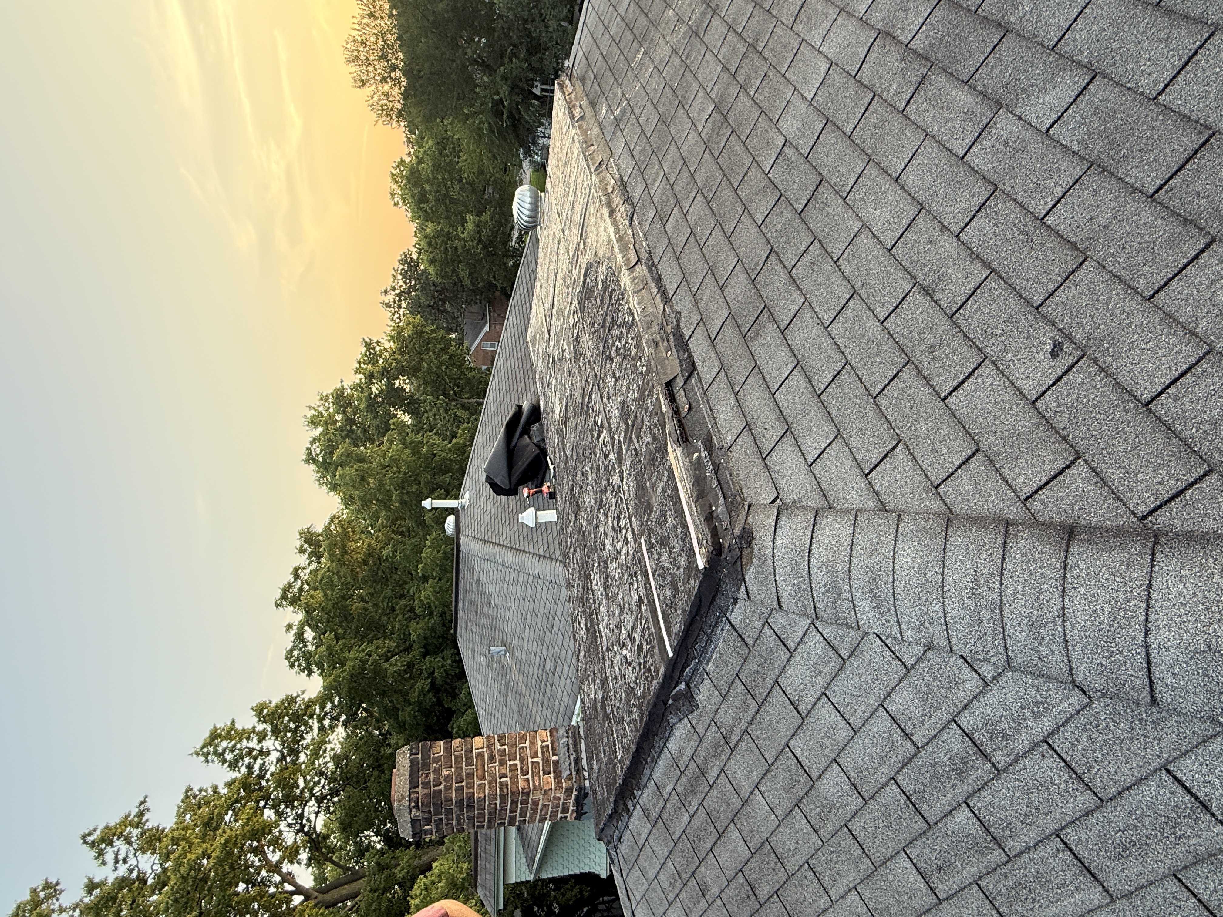 Aerial view of exposed roof deck near a brick chimney showing the stripped area from above