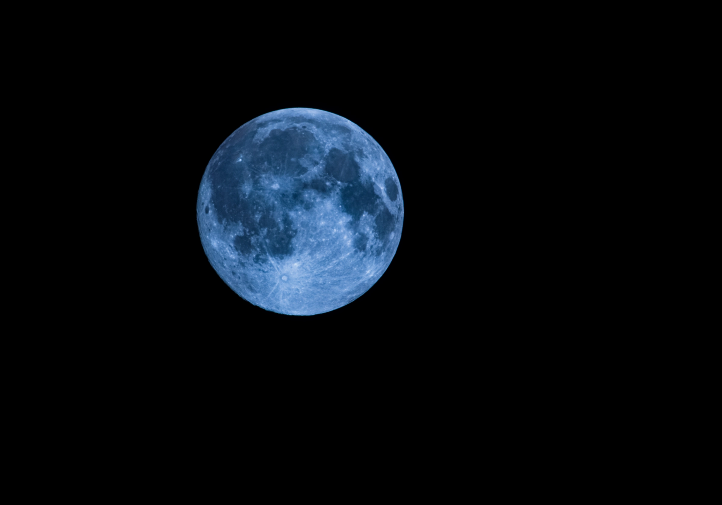 Detailed blue-toned photograph of the full moon against a black night sky, showing lunar craters, dark maria, and Tycho's bright ray system.