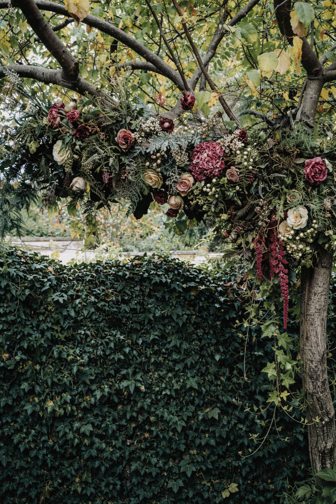 A floral arrangement hanging from a tree branch in front of an ivy-covered wall