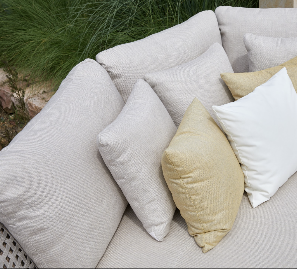 Daybed Alma en acabado Beige con cojines en tonos beige, ocre y blanco en contexto de jardín