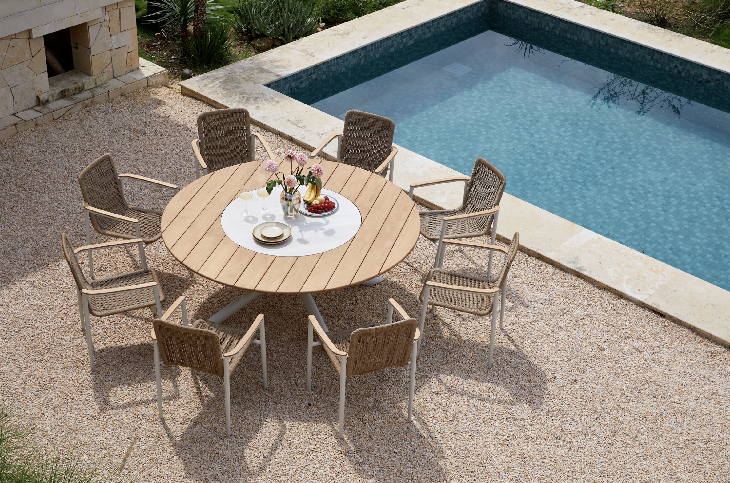 Comedor exterior con superficie de madera en terraza de grava junto a alberca
