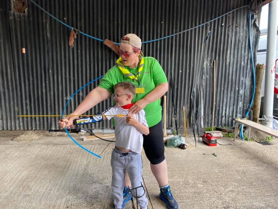 Leader helping a young Scout with archery