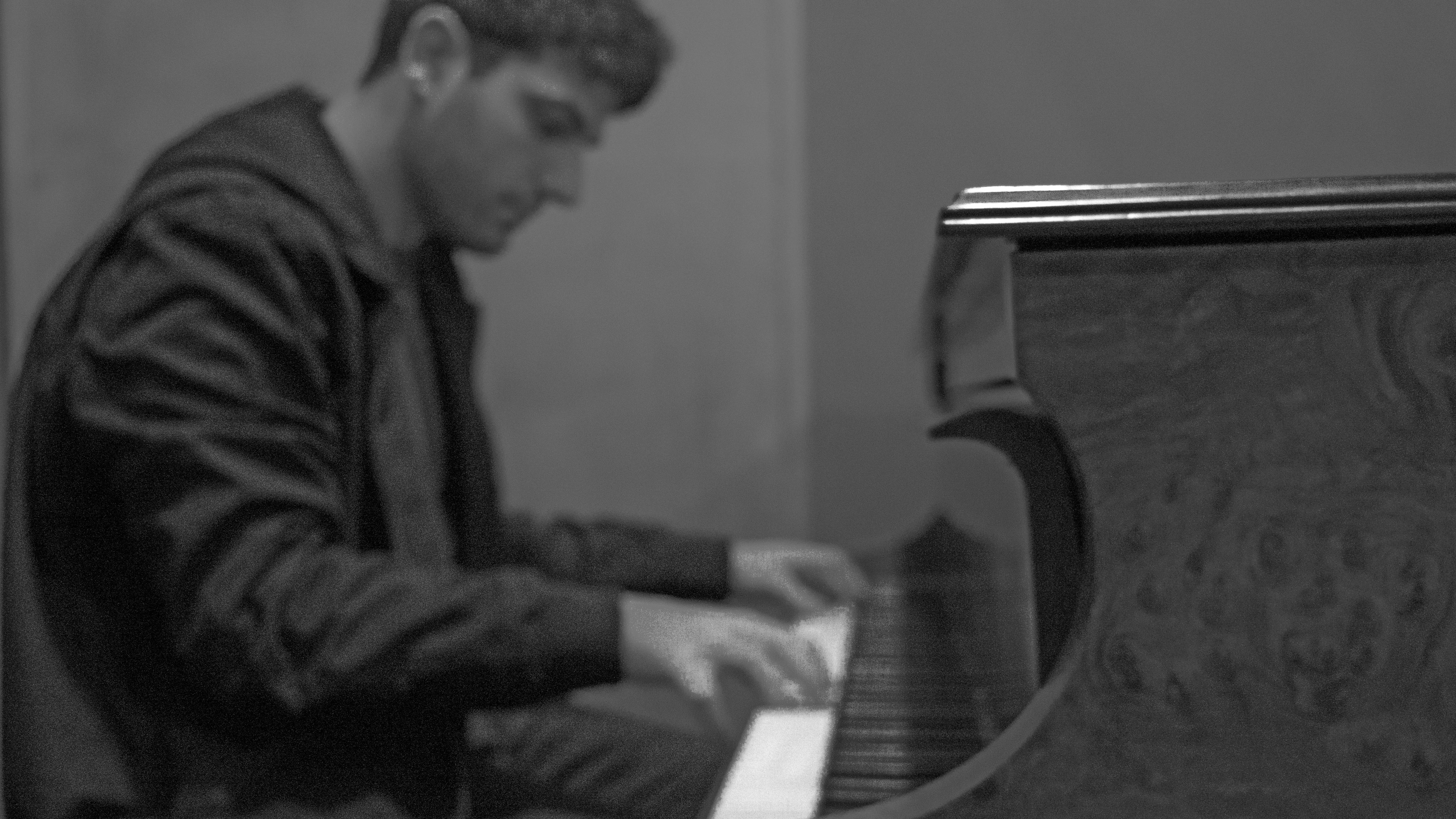 Side profile of a man playing an upright piano in black and white