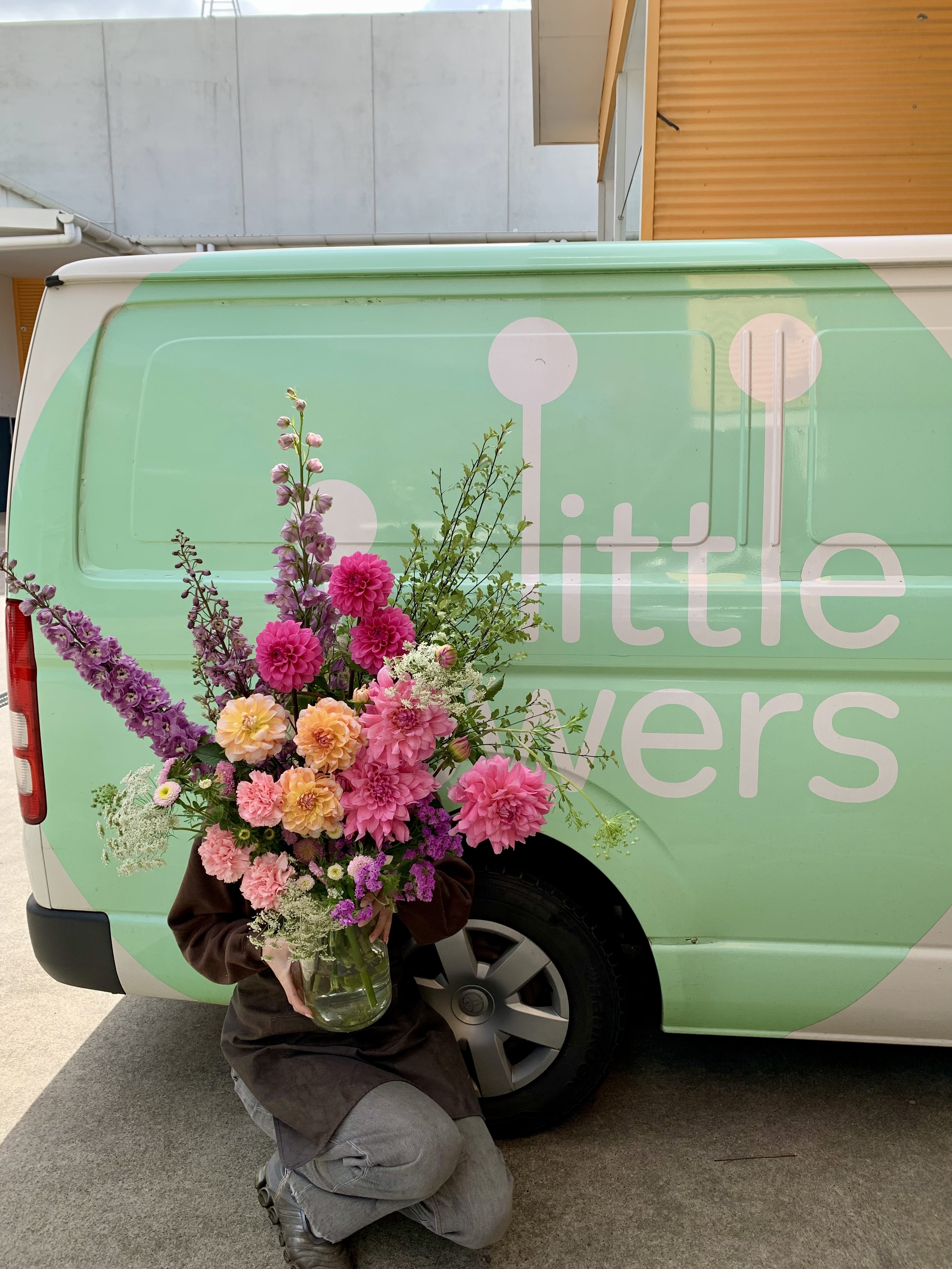 A Little Flowers grower holding a vibrant bouquet of event flowers beside the Little Flowers delivery van