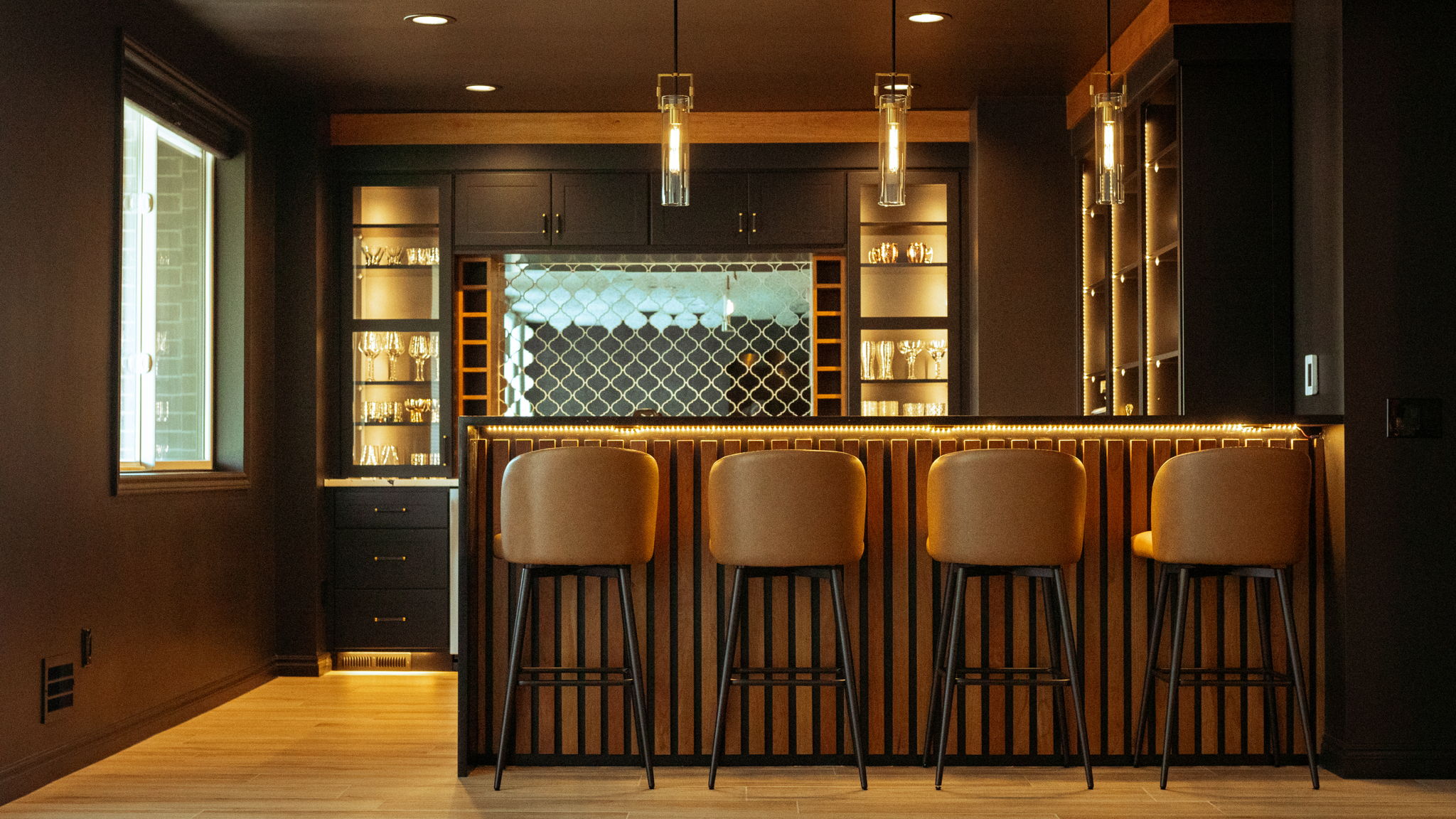 Moody wet bar with wood-slat front, matte black cabinetry, and warm LED accent lighting