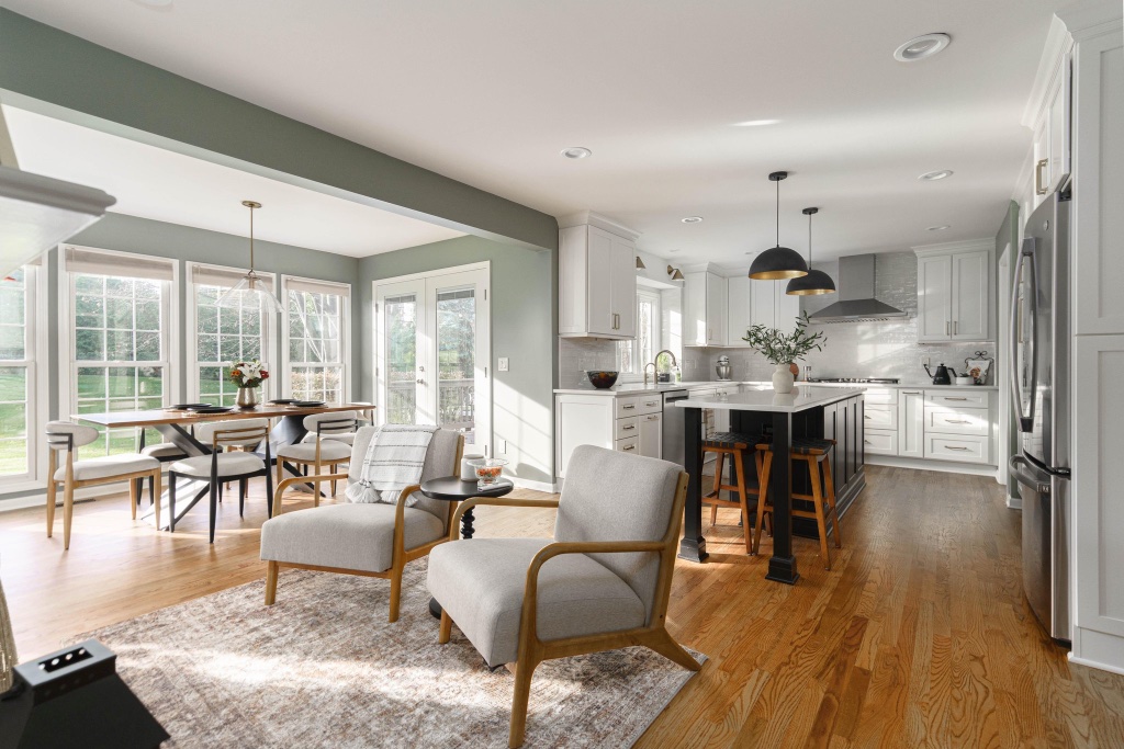 Open-plan kitchen with charcoal island, sage green walls, and brass pendant lights