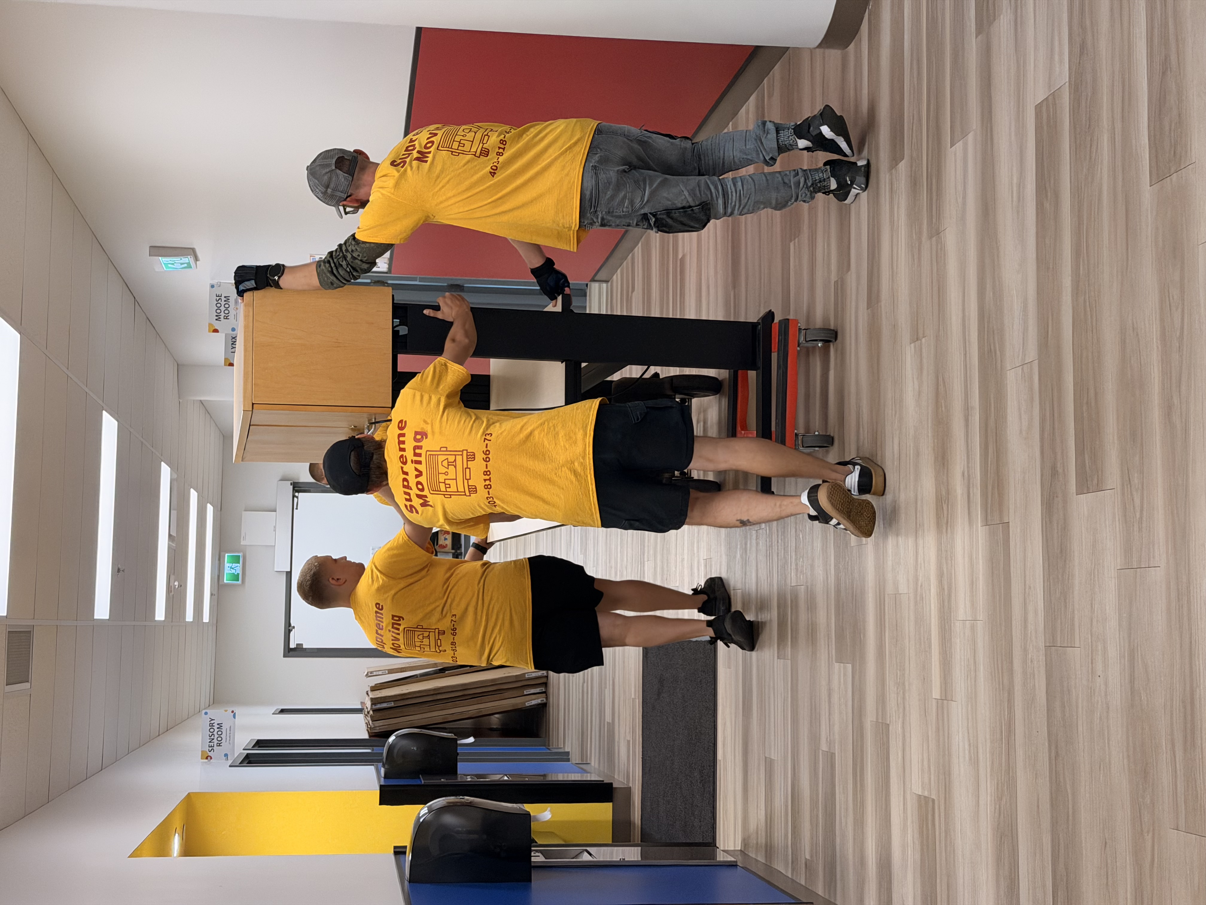 Three movers carrying a tall office cabinet