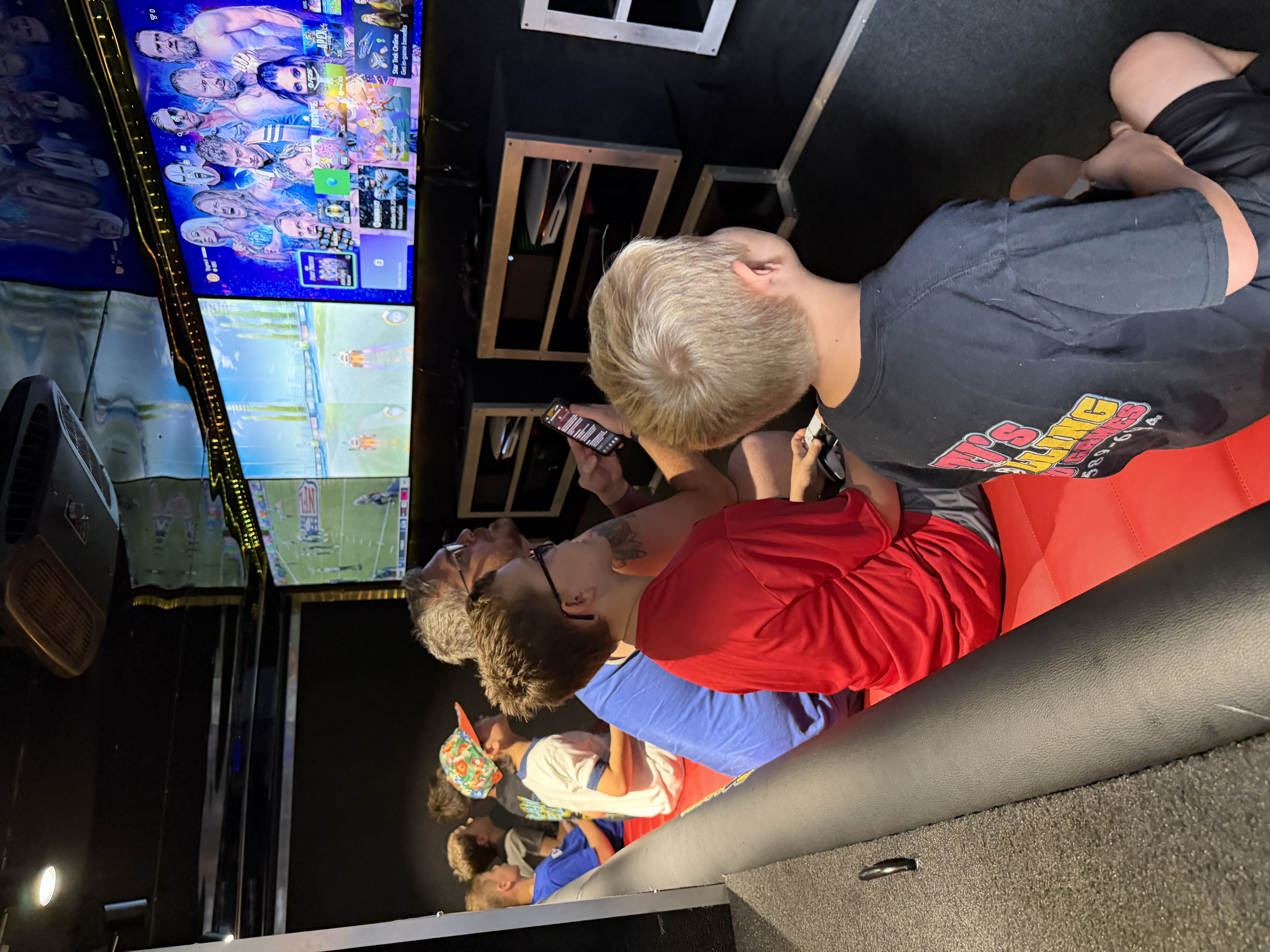 Kids and a parent inside the GameRush gaming truck, seated on the red bench and focused on the gaming screens