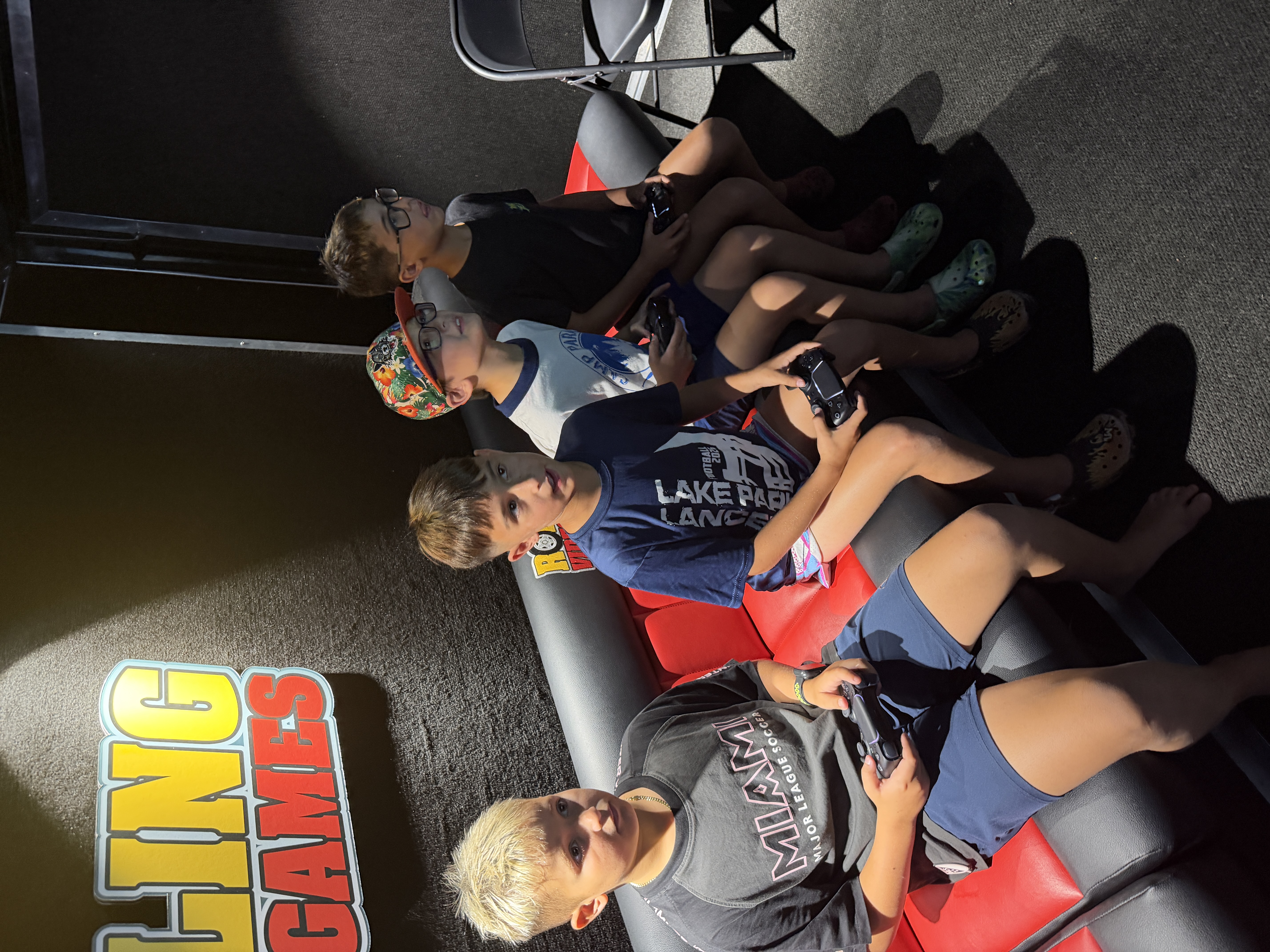 Four boys sitting on the tiered red and black bench inside the GameRush gaming truck, holding controllers and playing games together