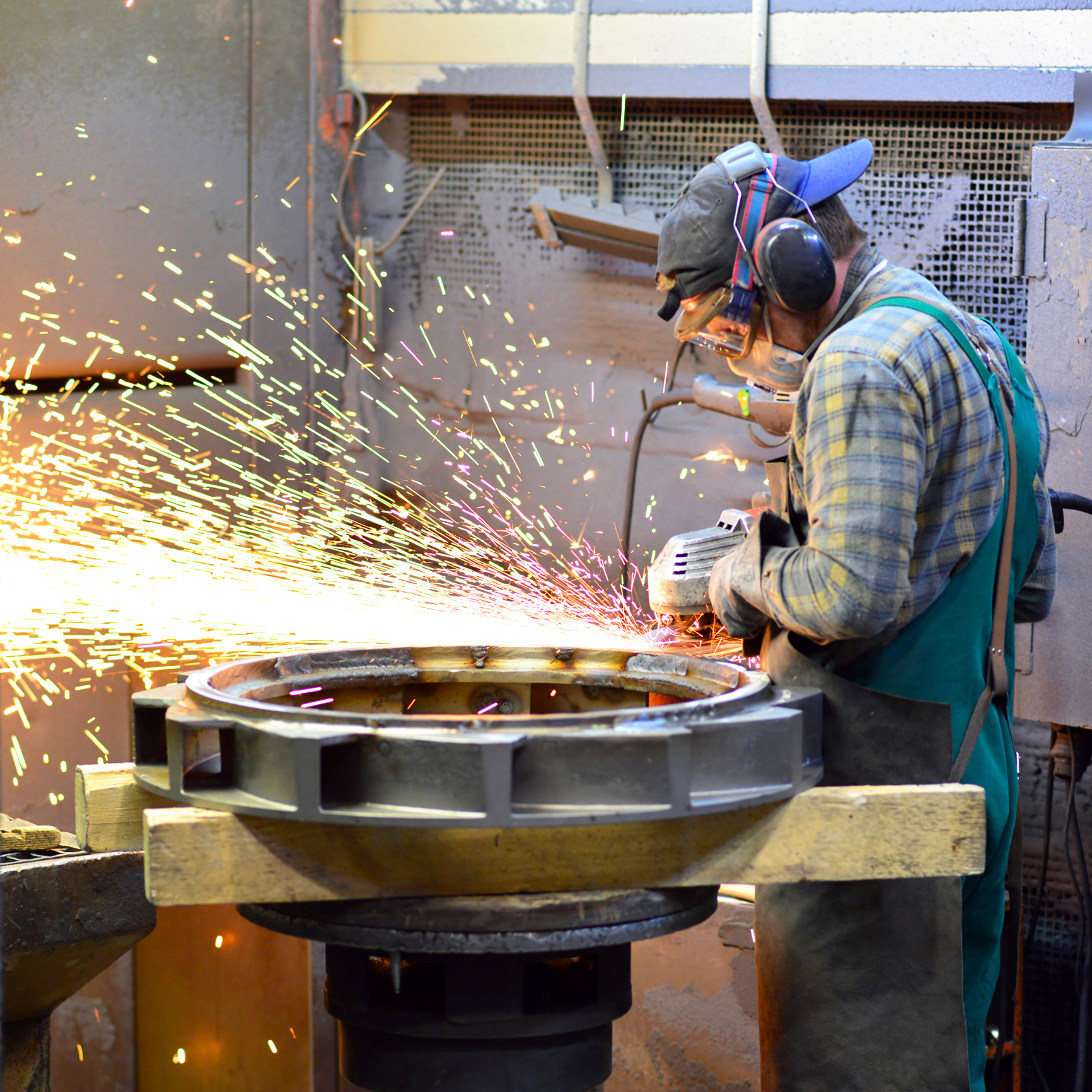 Tradesperson grinding a metal fabrication with sparks flying in a workshop