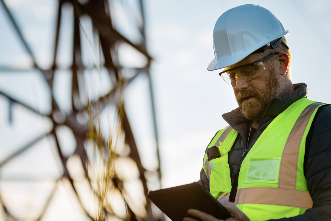 Construction professional using a tablet while wearing a hard hat and safety vest