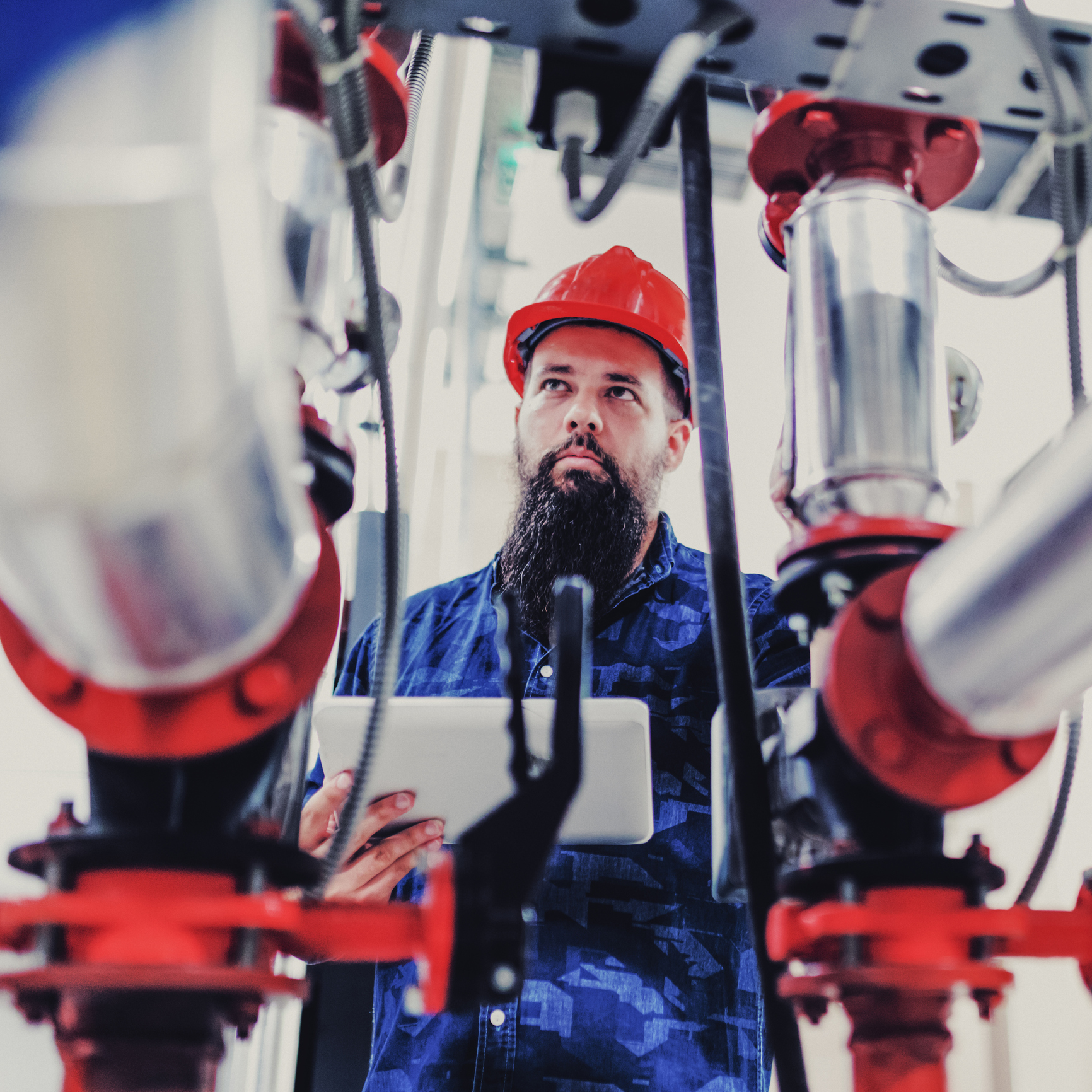 Plumbing technician reviewing a tablet beside large red valve piping in a mechanical room