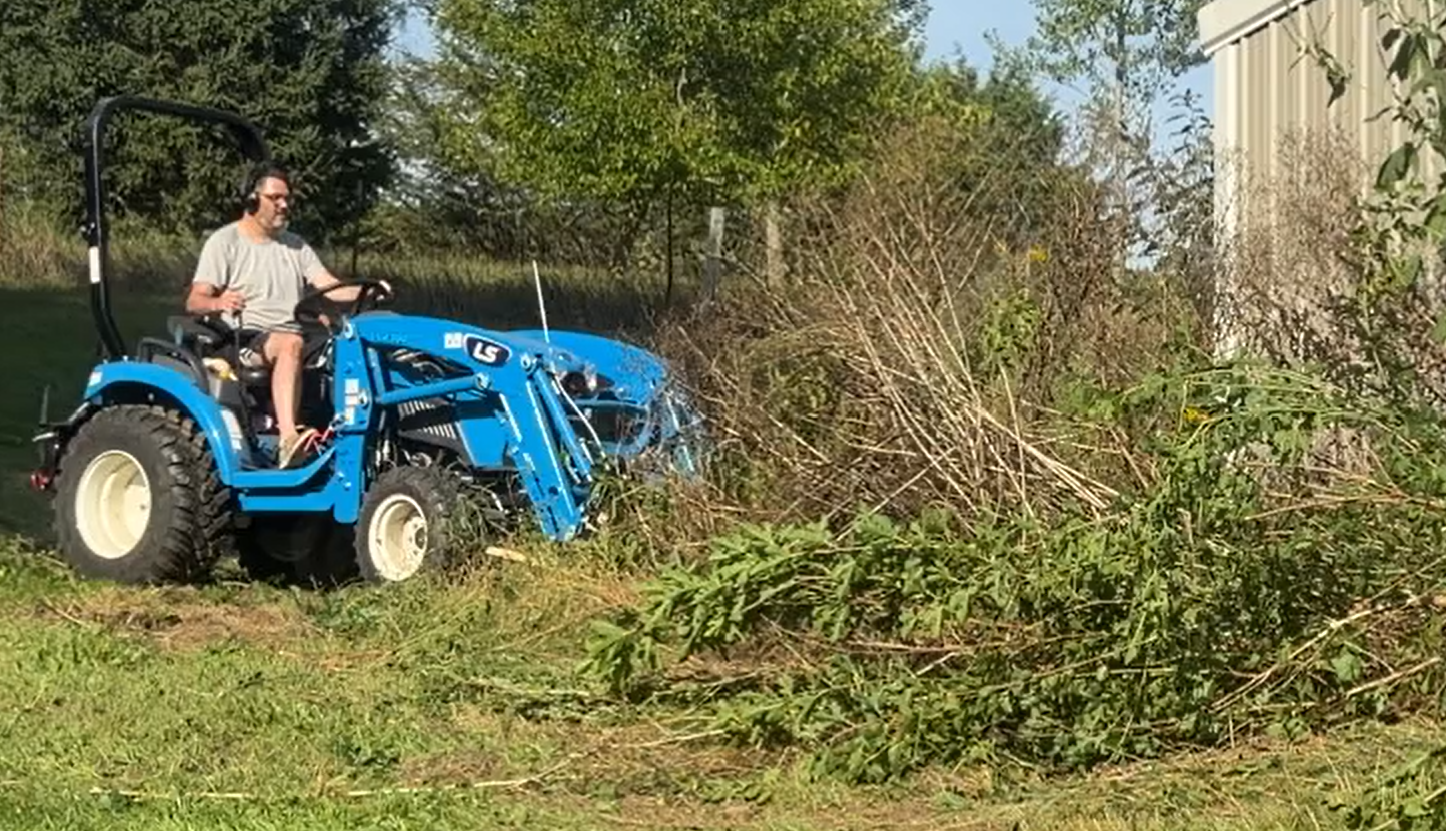 LS compact tractor clearing brush and debris in a grassy yard