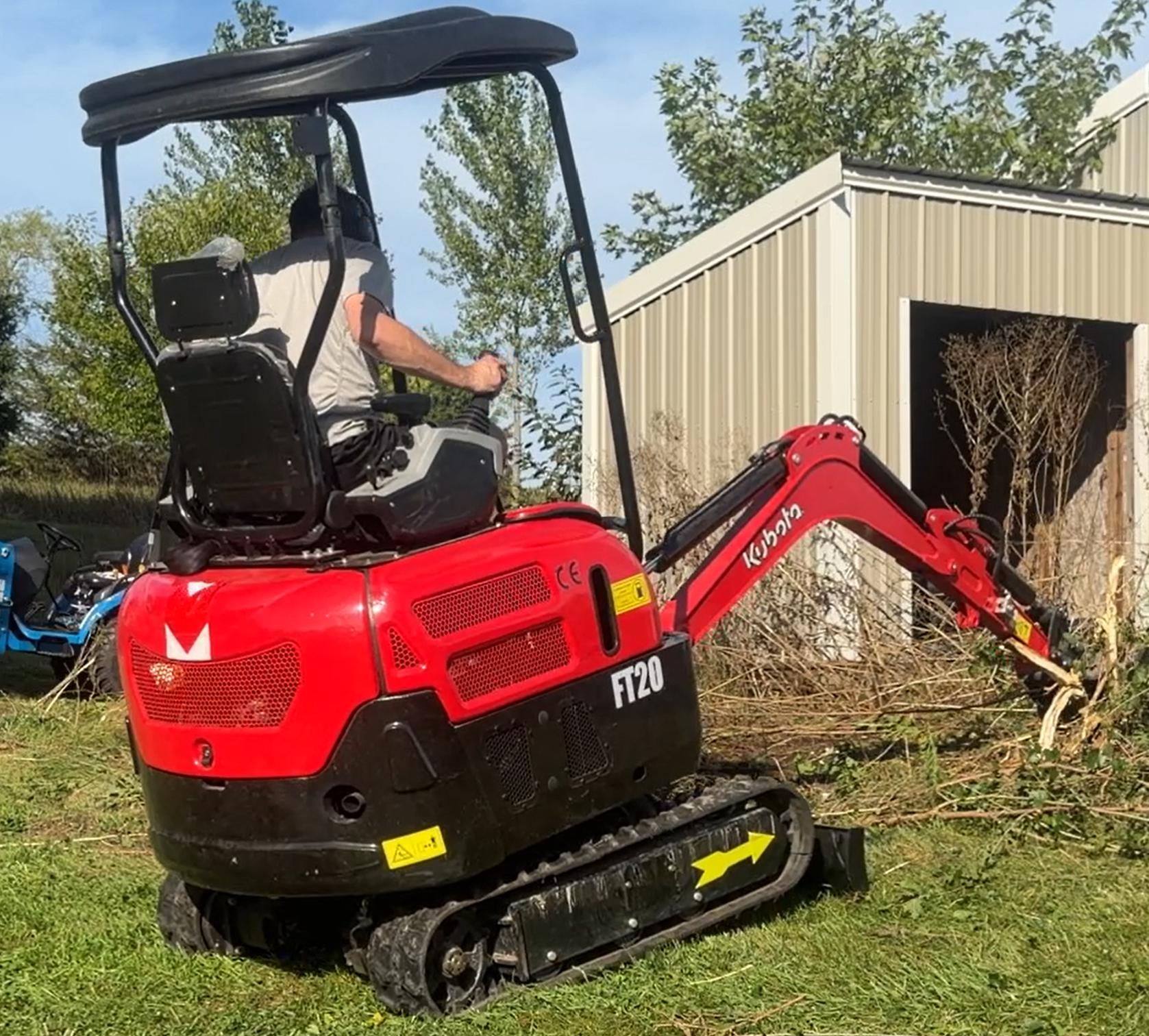 Kubota FT20 compact excavator at work clearing brush near a utility building