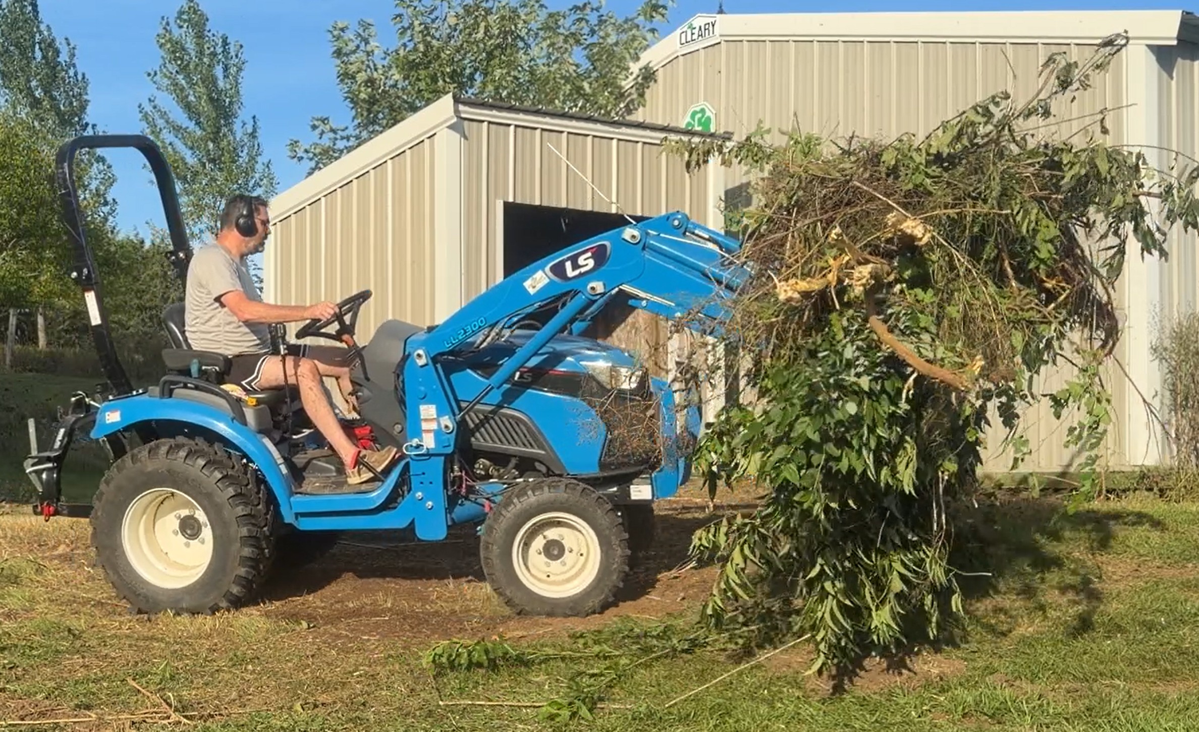 LS LL2300 tractor with raised loader carrying a pile of cut branches on a lawn