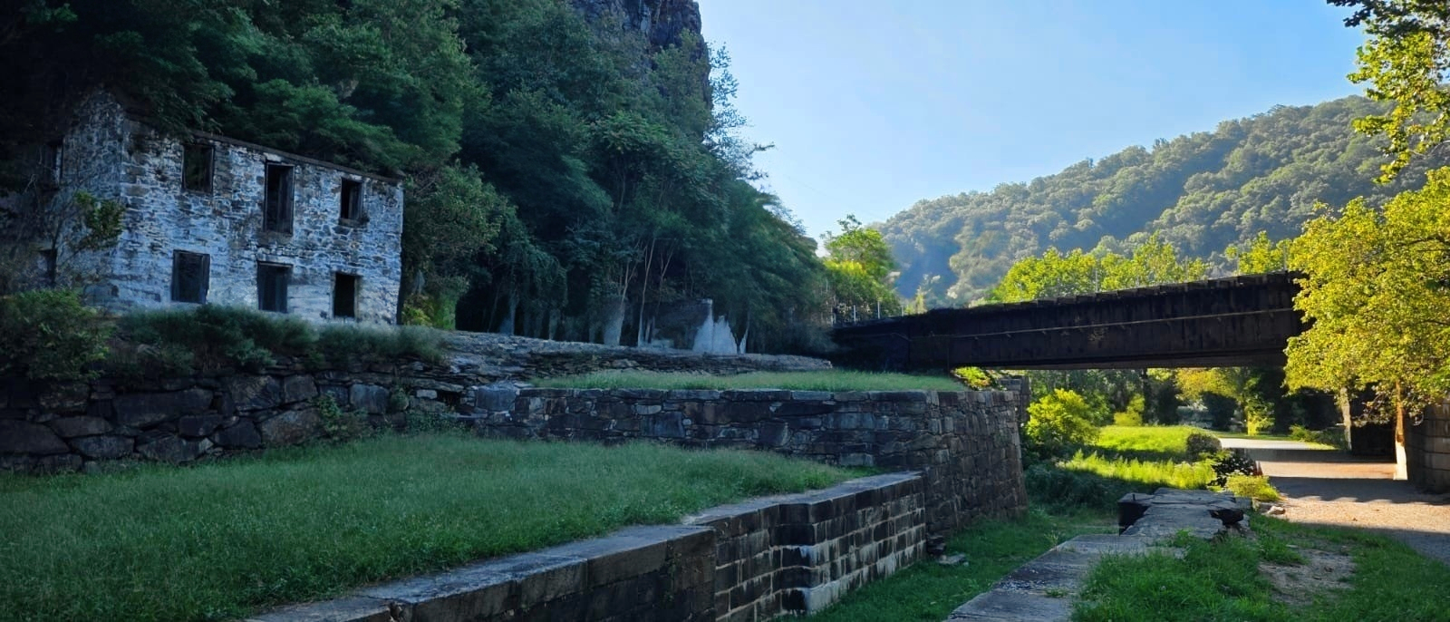 Canal lock ruins and a railway bridge at Harpers Ferry — the stonework of the canal Mercer championed, still standing beneath the later iron that crossed it.