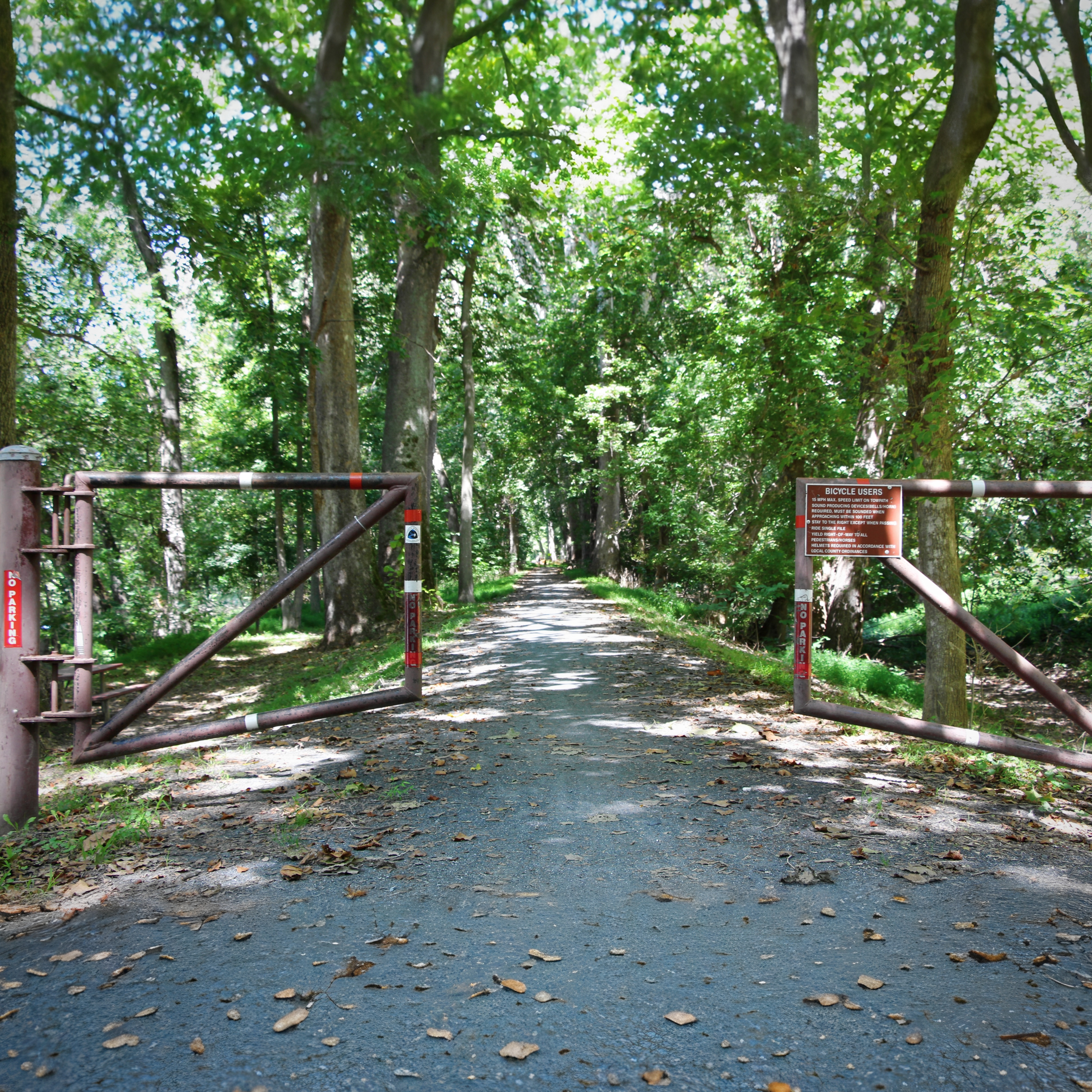 The towpath at Brunswick, framed by its gates — the gravel lane the mules once walked, now signed for the cyclists and walkers who inherited it.