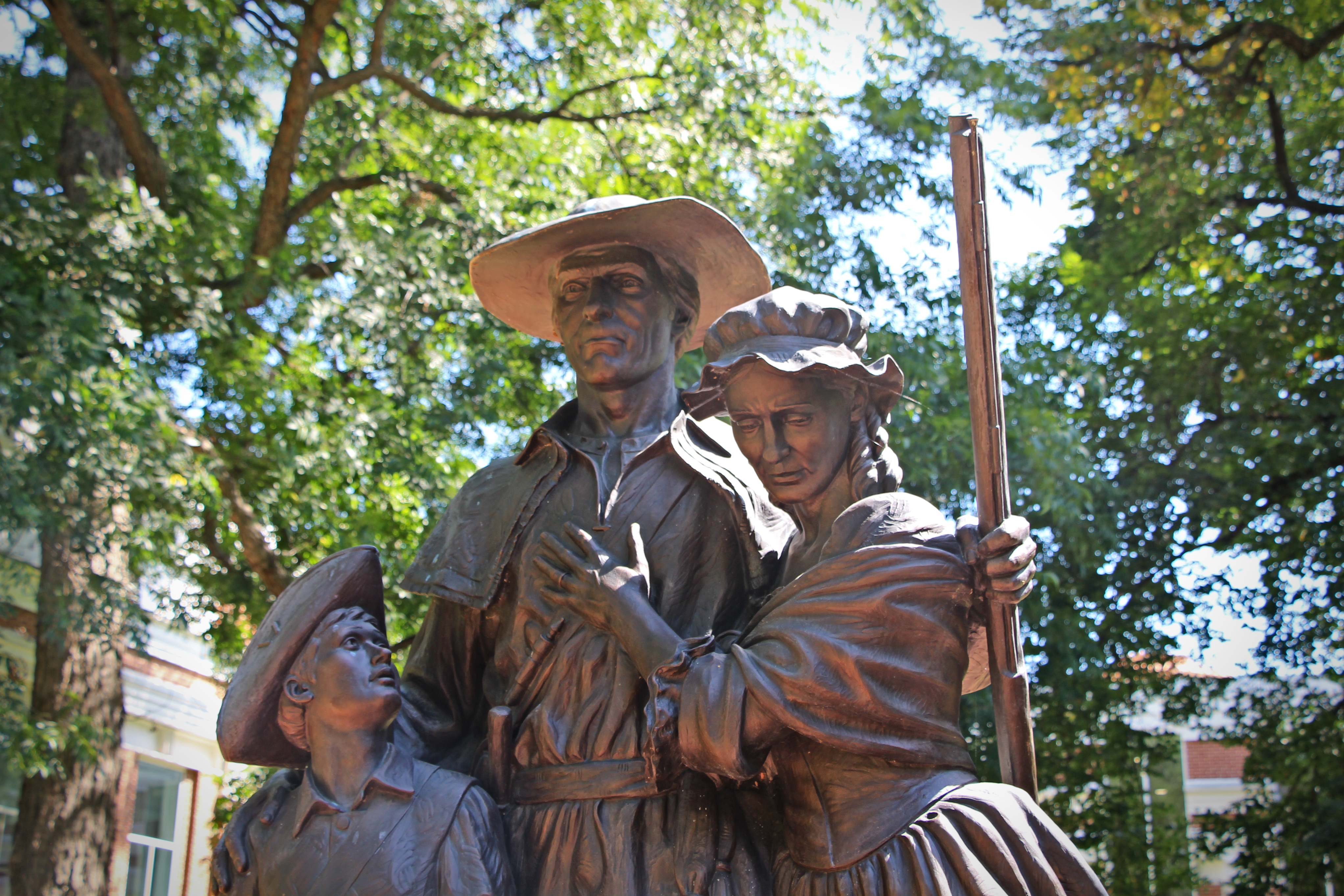 A bronze family stands outside the courthouse — figures out of the very century the series inhabits.