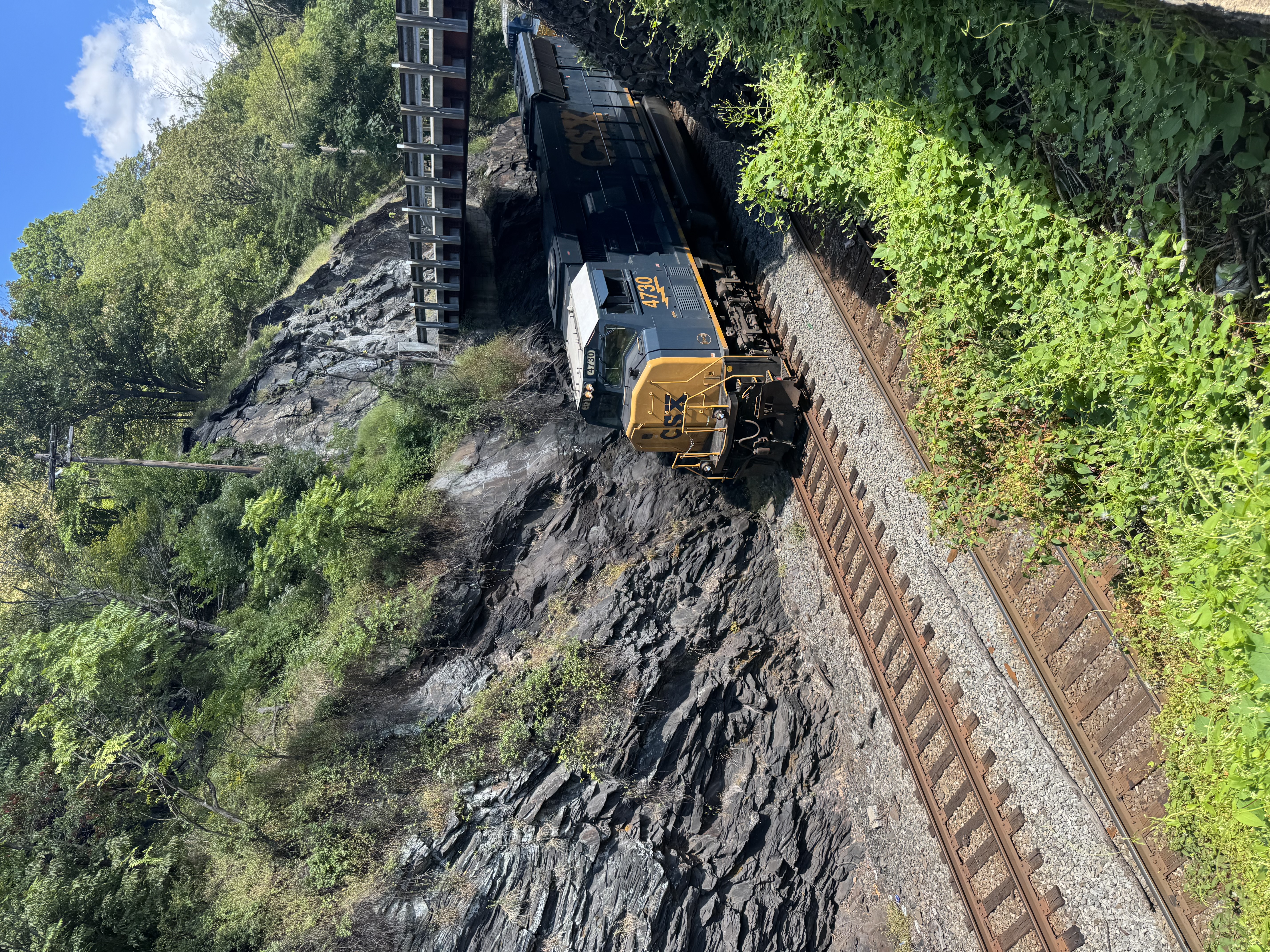 A freight threading the rock cut above the river — the same corridor the canal opened, now running on steel.