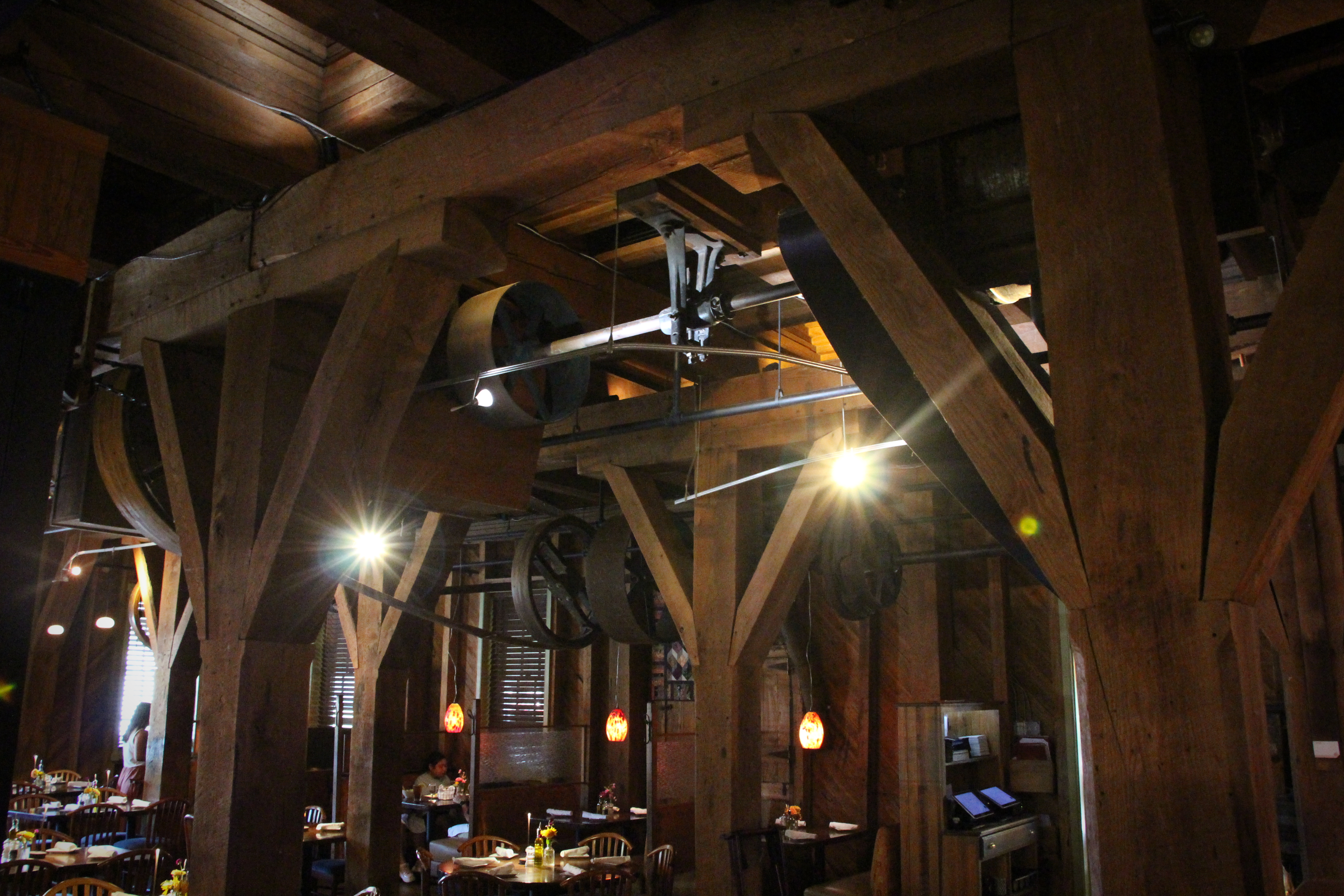 Linen-set tables sit beneath the gears — the mill’s working bones still overhead.