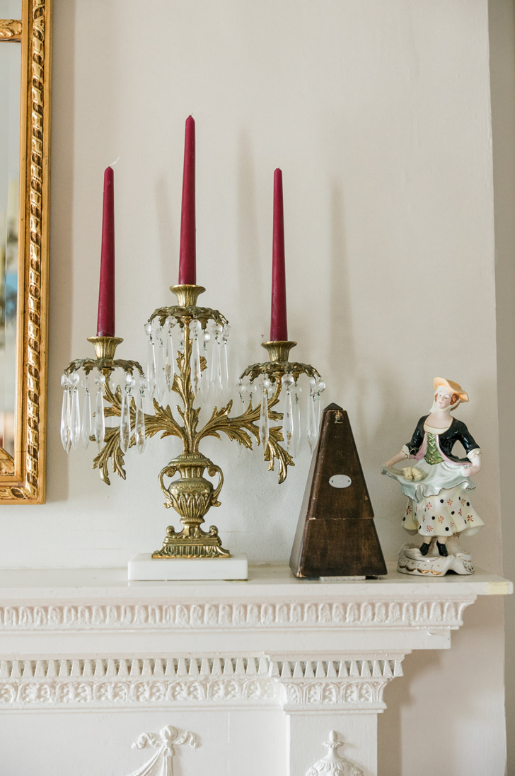 Detail of the Lafayette Parlor mantel — brass candelabra, a metronome, and a porcelain figurine arranged on the carved shelf.