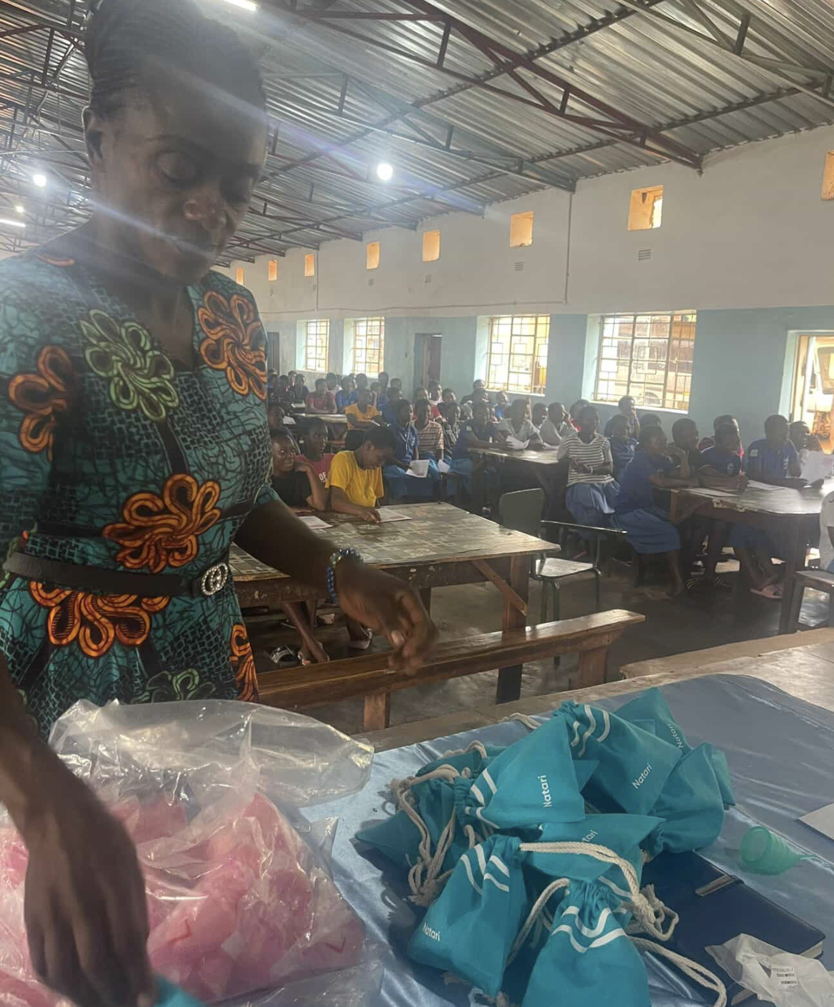 A volunteer unpacking Natari menstrual cup pouches in front of a classroom of students