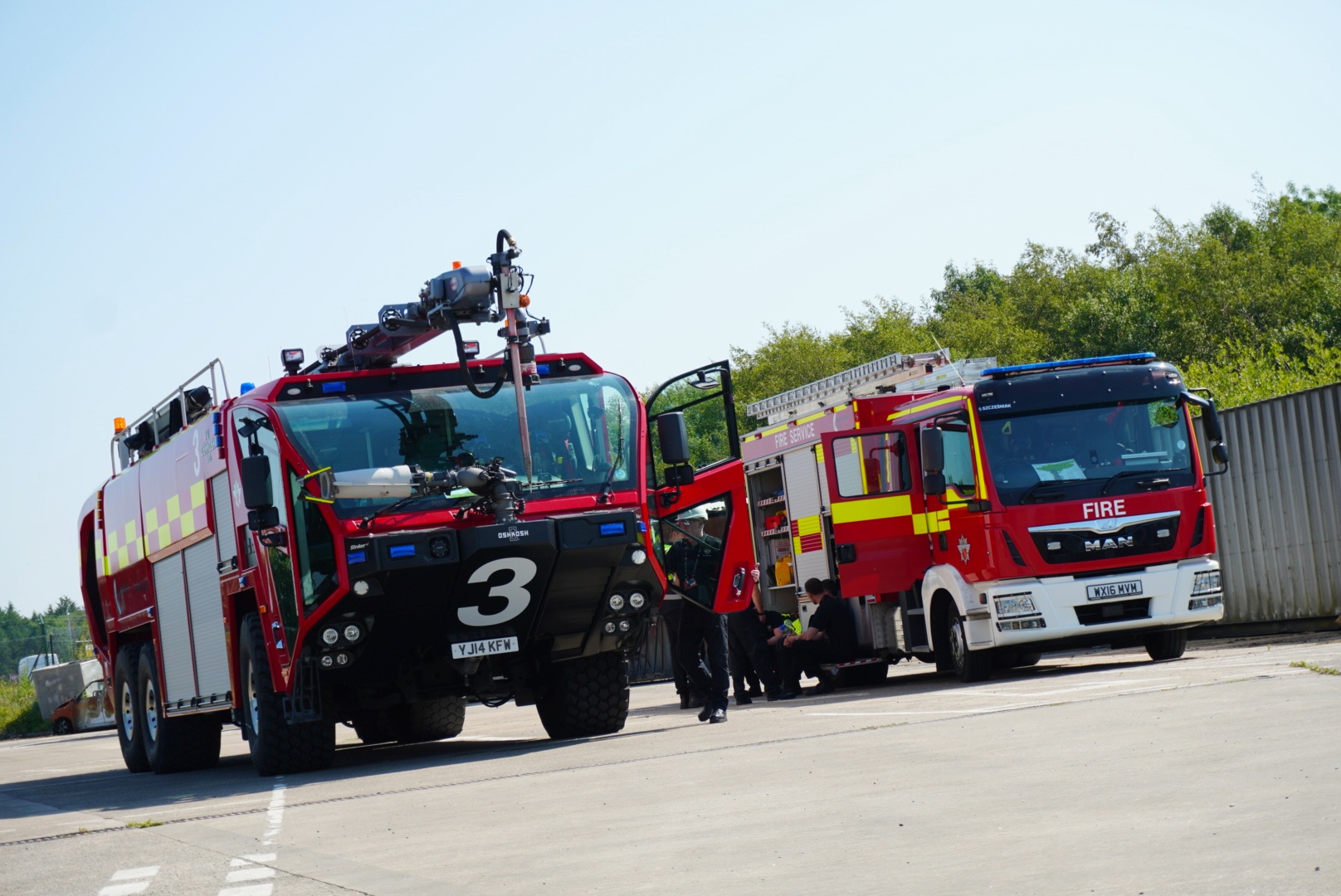An Oshkosh Striker ARFF vehicle and the MAN domestic pump appliance stand ready for training drills.