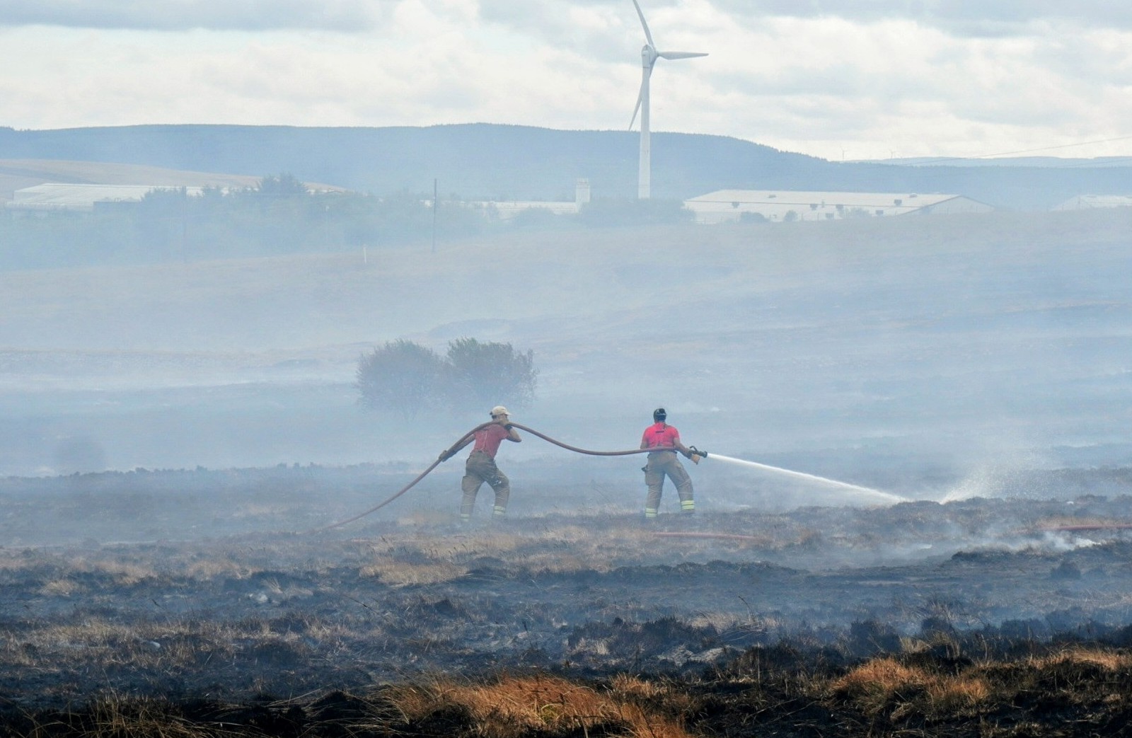 Firefighters working hose lines across scorched moorland