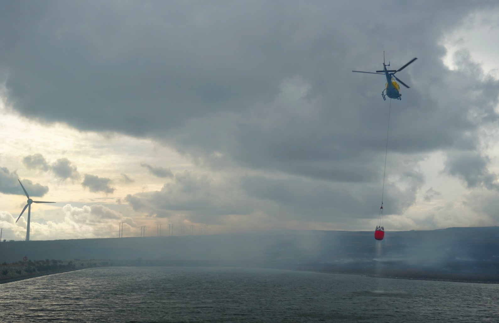 A helicopter with a Bambi bucket working over a reservoir during the summer 2026 wildfire response