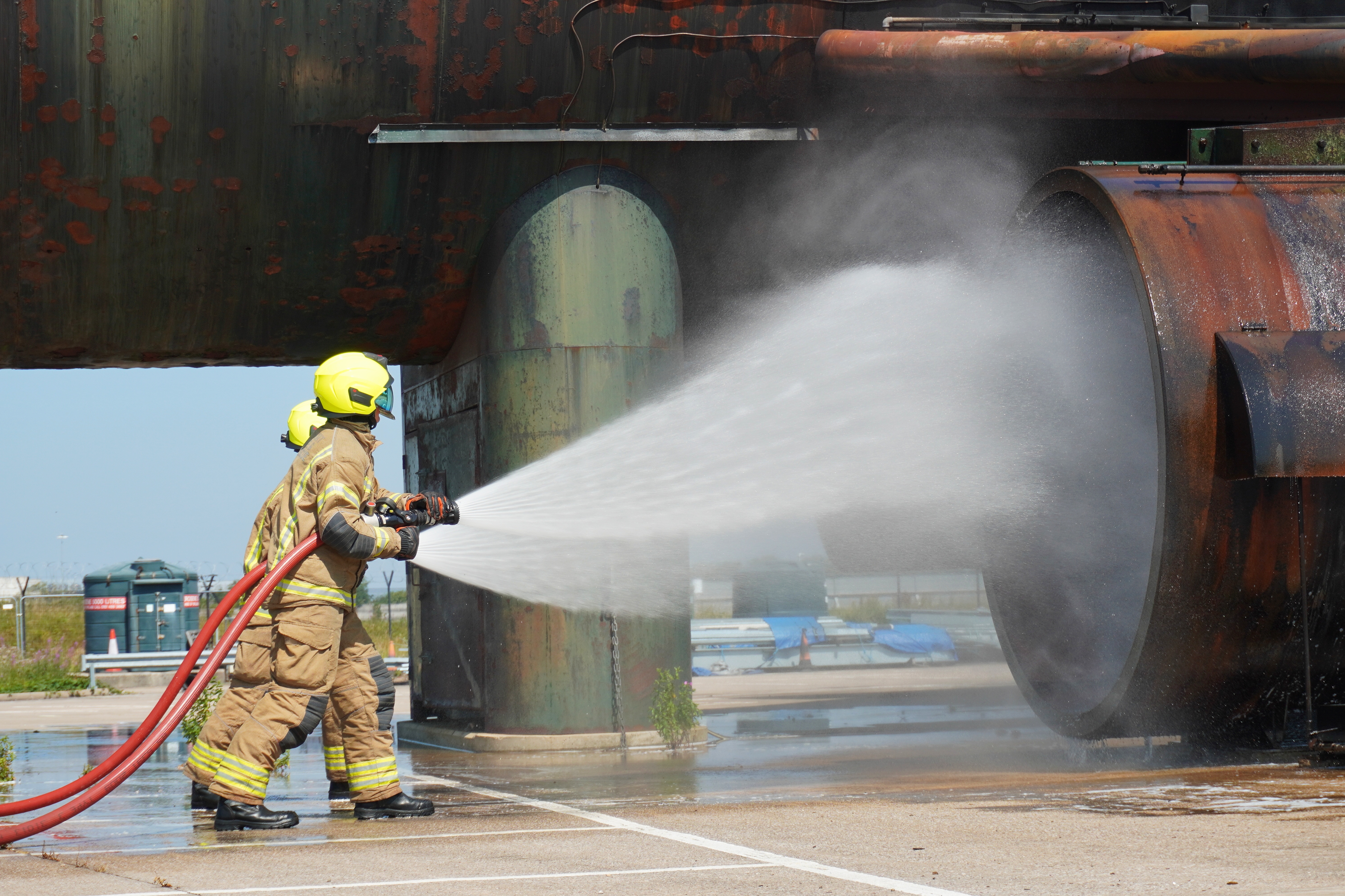 Firefighters direct a jet of water onto a simulated engine fire on the large aircraft firefighting rig.