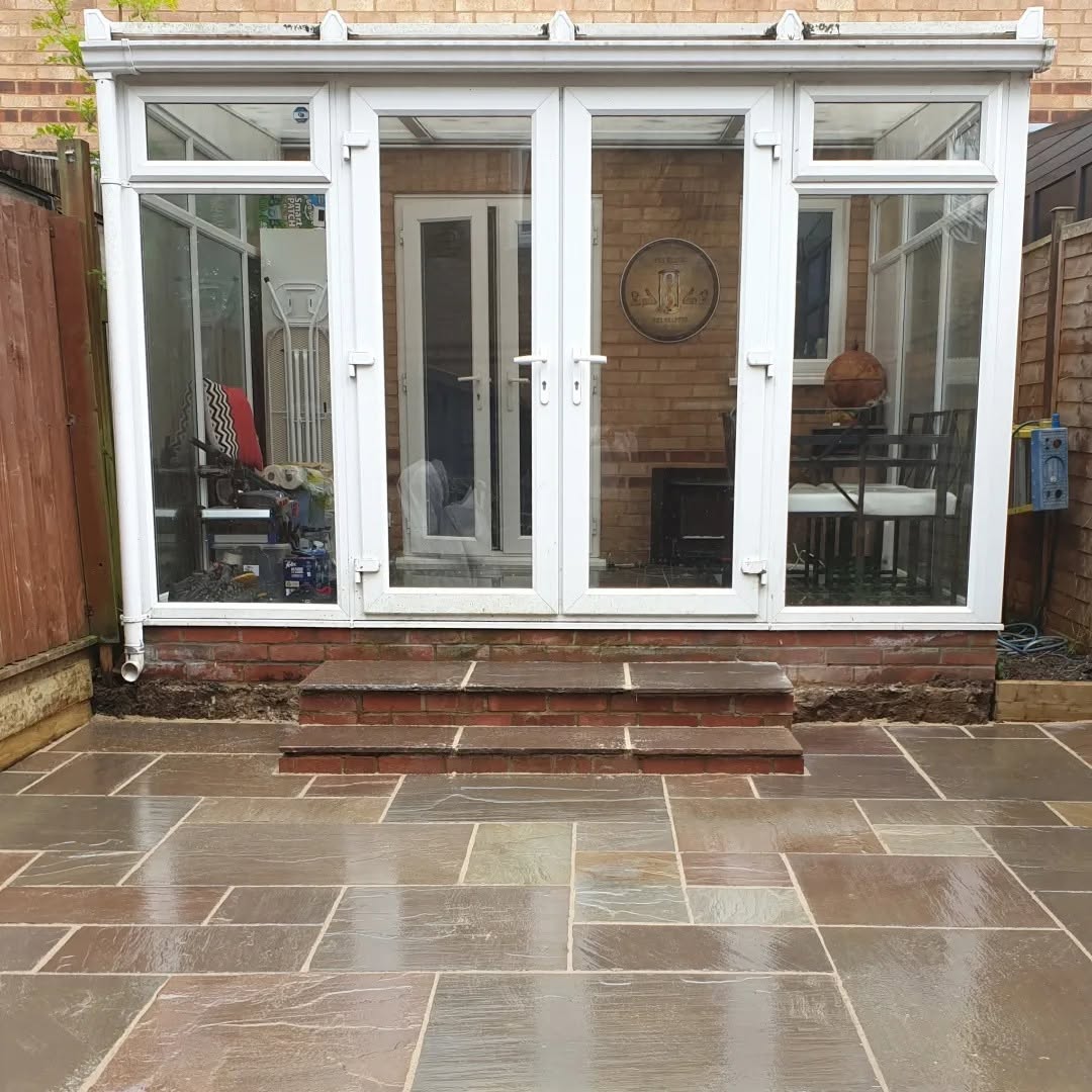 New stone patio with brick steps leading up to the conservatory by Timmins Landscapes