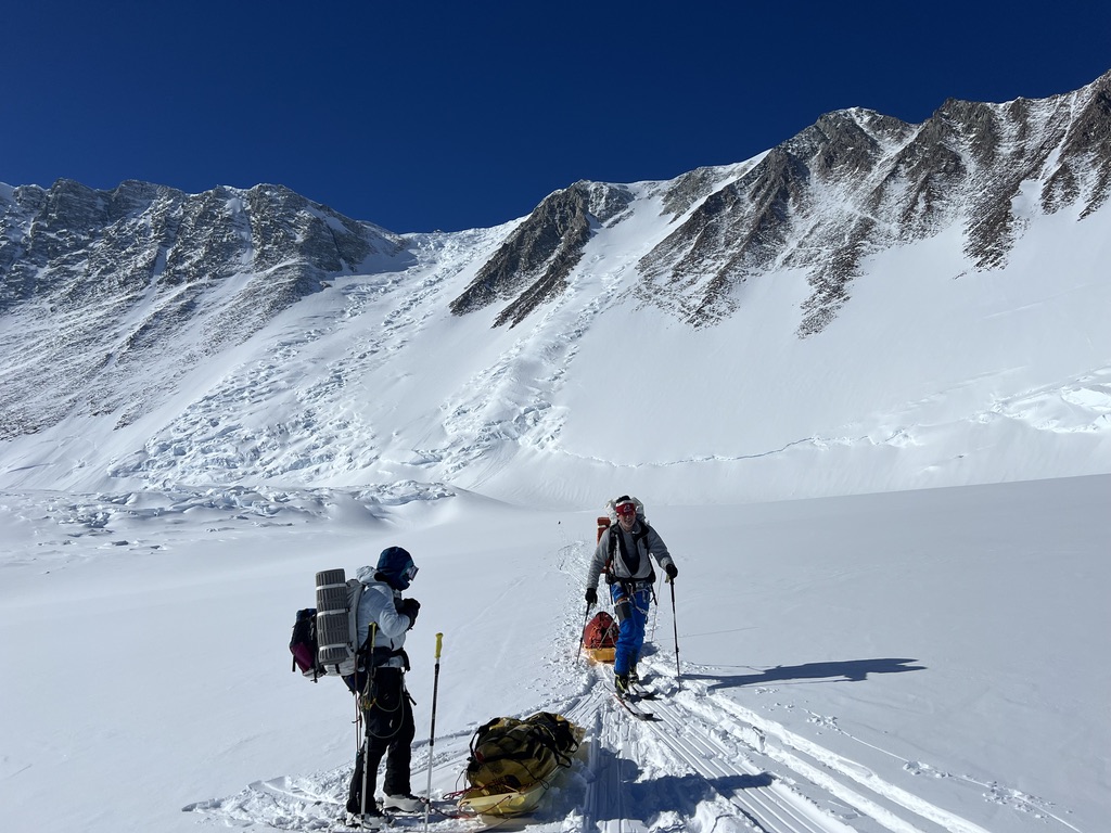 Sea-to-ski group skinning up Svalbard peak with icy fjord and glaciers below