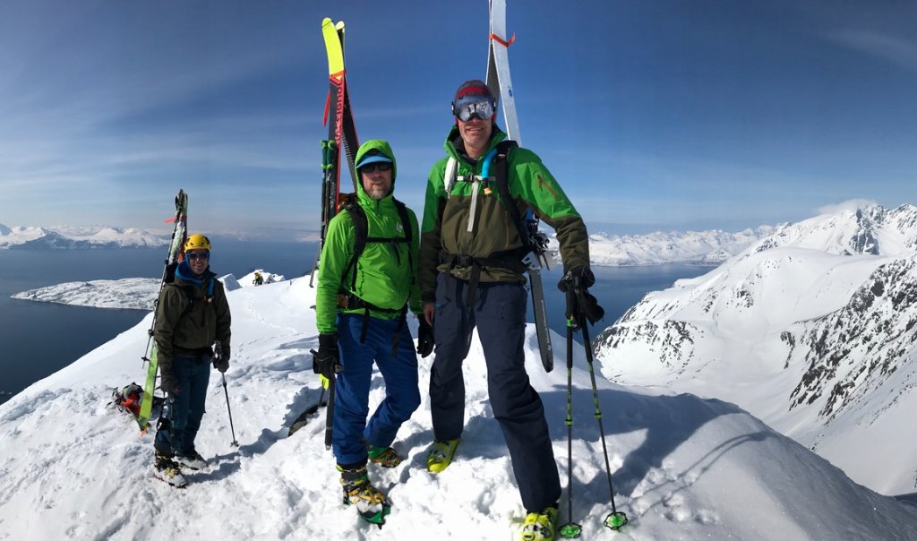 Group of three backcountry skiers posing on Lyngen Alps summit ridge above fjord