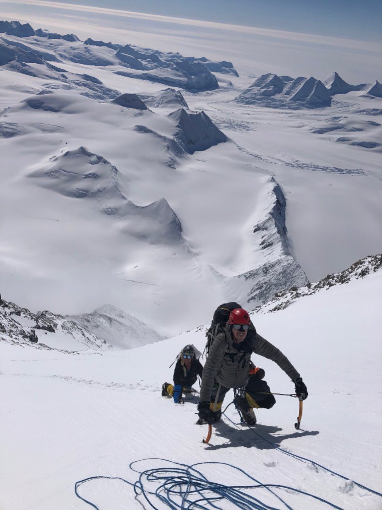 IFMGA guide bootpacking with skis on Svalbard summit ridge above ice-filled fjord