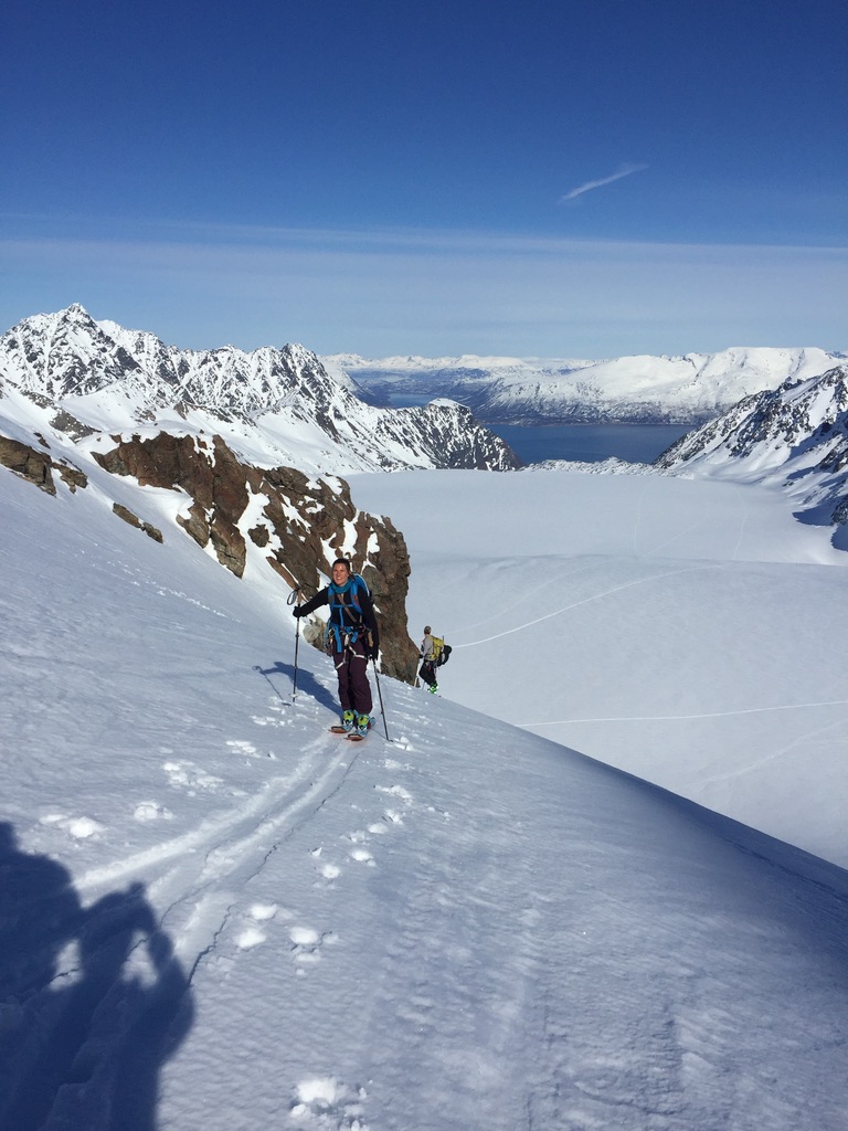Ski tourer traversing steep snowy slope above Lyngen Alps fjord, Norway