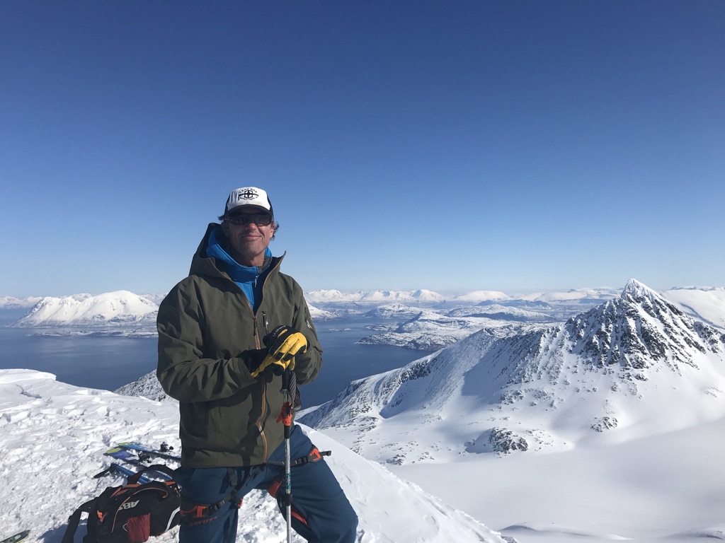 Skier at Lyngen Alps summit with skis and fjord panorama, Arctic Norway