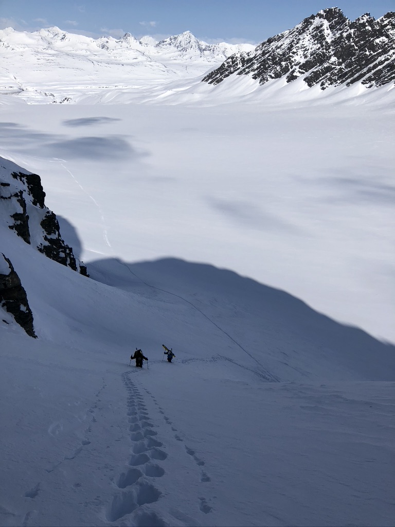 IFMGA guide bootpacking with skis on Svalbard summit ridge above ice-filled fjord