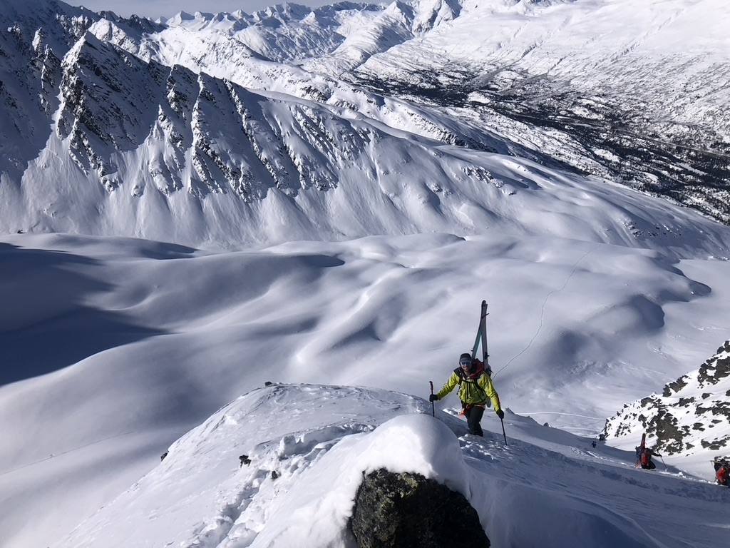 Sea-to-ski group skinning up Svalbard peak with icy fjord and glaciers below