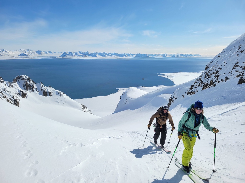 Ski mountaineers ascending steep couloir above Arctic sea in Svalbard, Norway